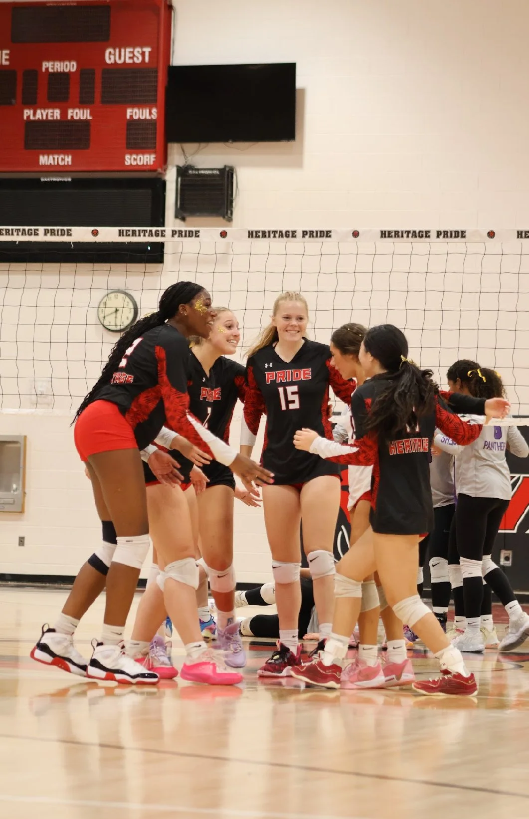 Girls' volleyball team celebrating on the court with Nike athletic shoes, kneepads, and uniforms with 'PRIDE' on the front.