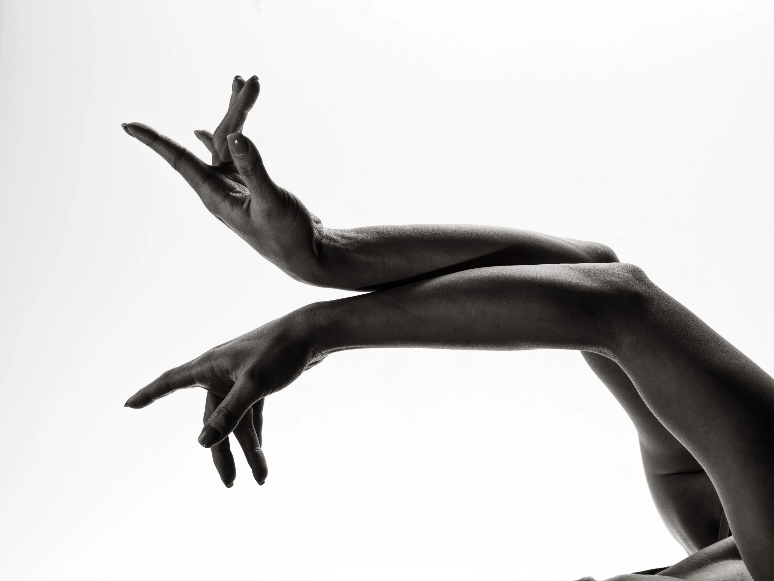 Black and white photo of two hands gracefully posed, with fingers extended and intertwined, against a plain background.