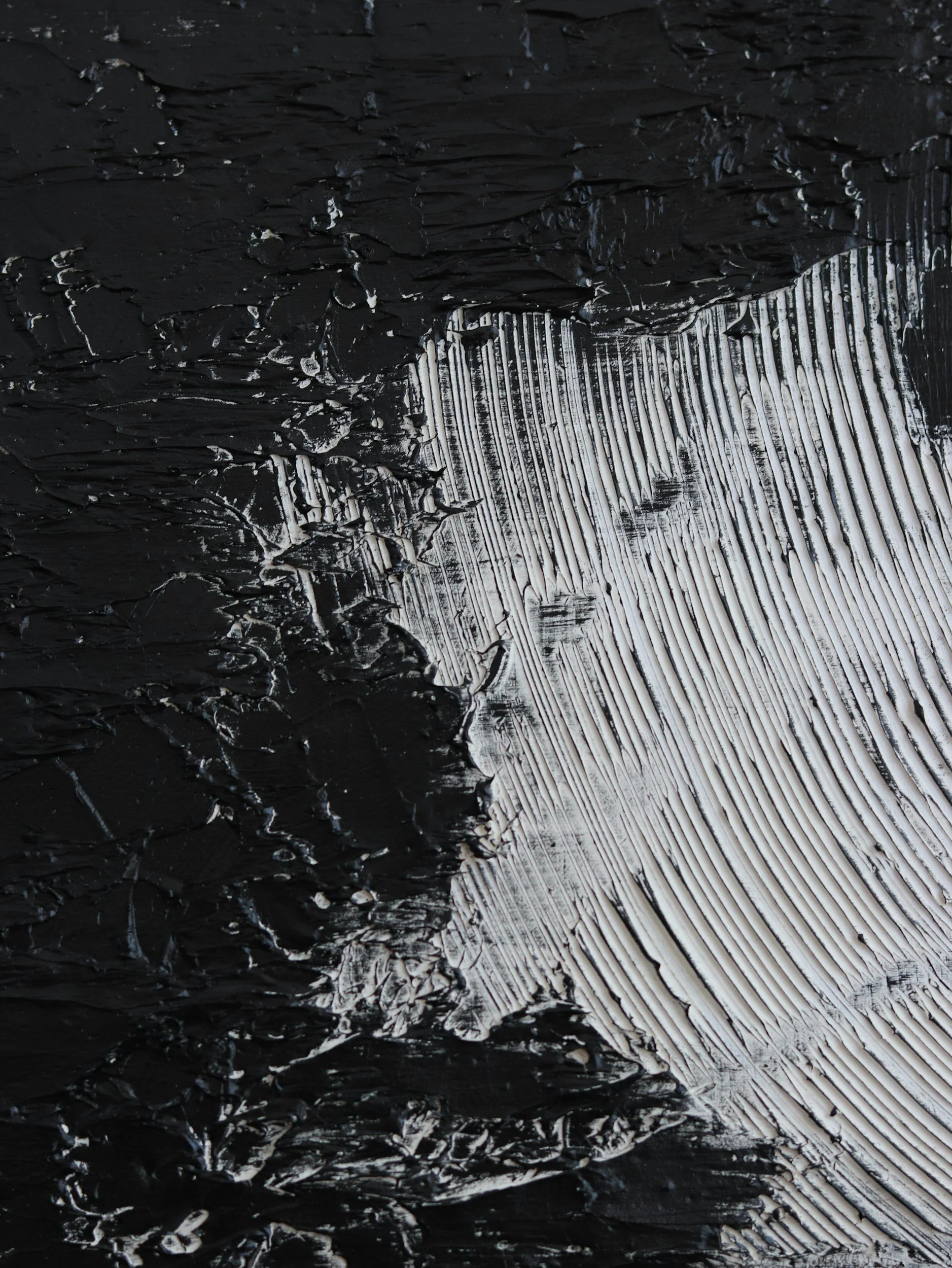Close-up of black and white textured paint with thick black strokes on the left and white, turquoise, and silver lines on the right.