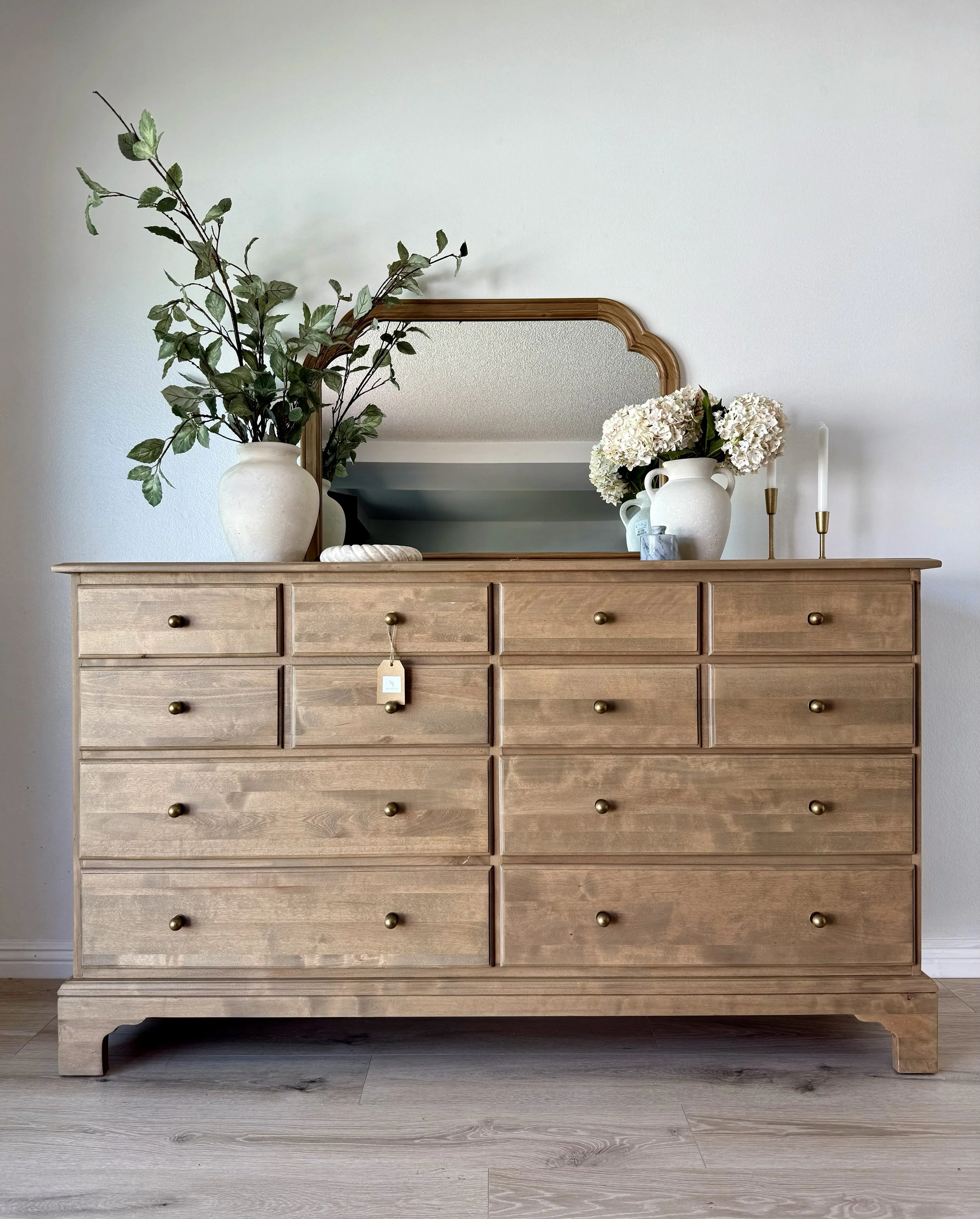 Wooden dresser with a mirror, decorated with vases of flowers and candles on top.