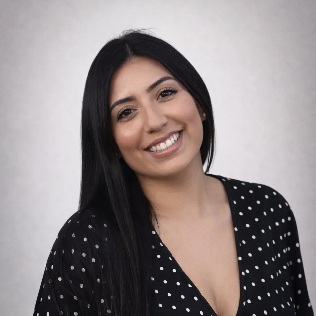 A young woman with long black hair, smiling, wearing a black top with white polka dots, against a plain light background.