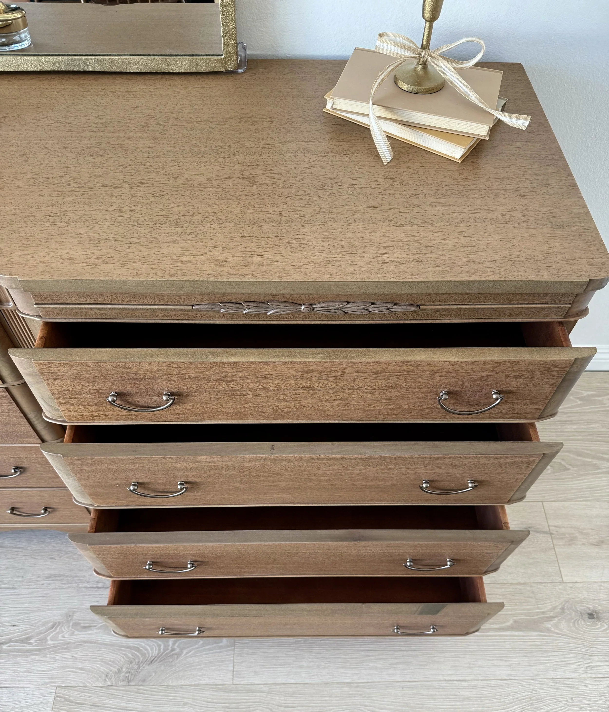 Top view of a wooden dresser with four open drawers, a decorative lamp with books on top, and part of a mirror and a white wall.