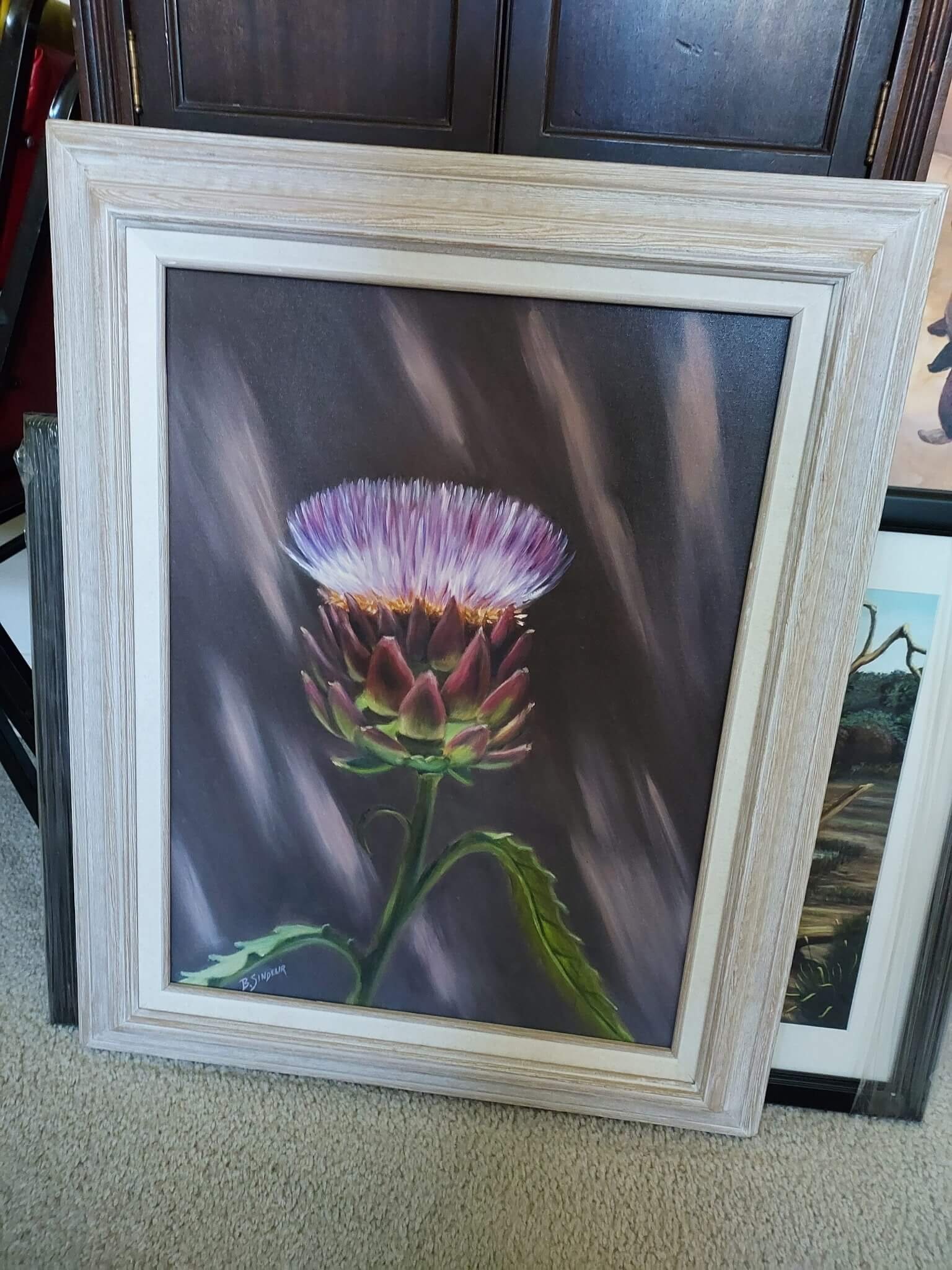 A framed painting of a purple and white flower with green leaves on a dark background.