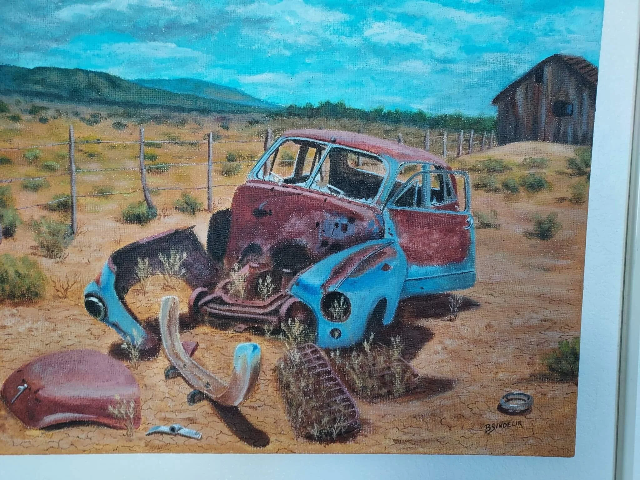 A painting of an abandoned, rusty, and broken-down blue and red car in a desert landscape with dry grass and plants, a wire fence, a hill, and a barn in the background.