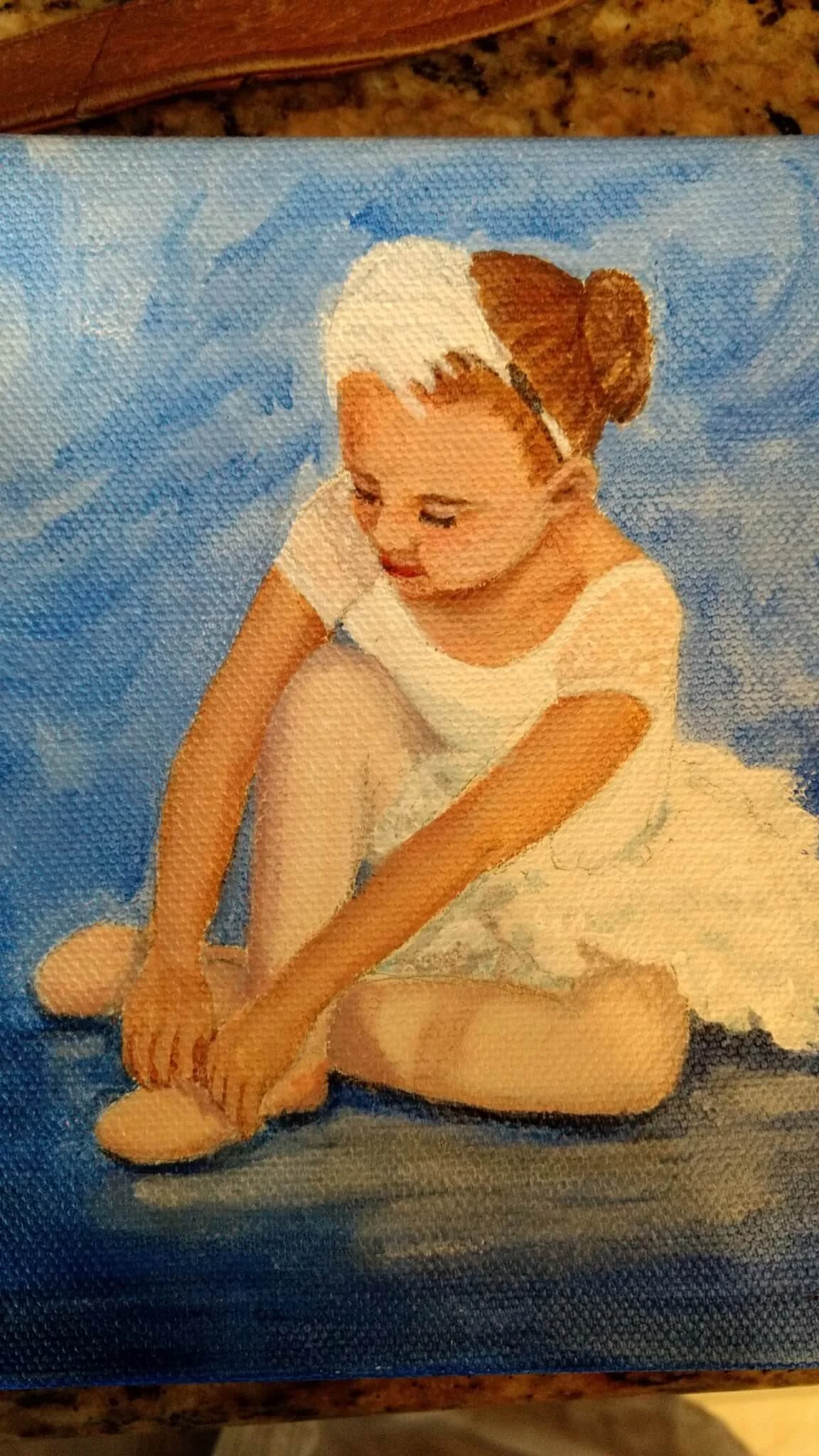 A girl with brown hair tied in a bun, sitting on a blue background, wearing a white dress and white tights, tying her ballet shoes.