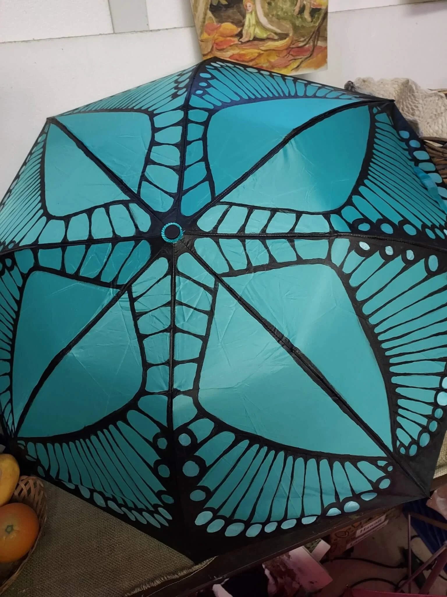 A teal and black umbrella with a spiderweb and spider design, positioned on a table among fruits and other items.
