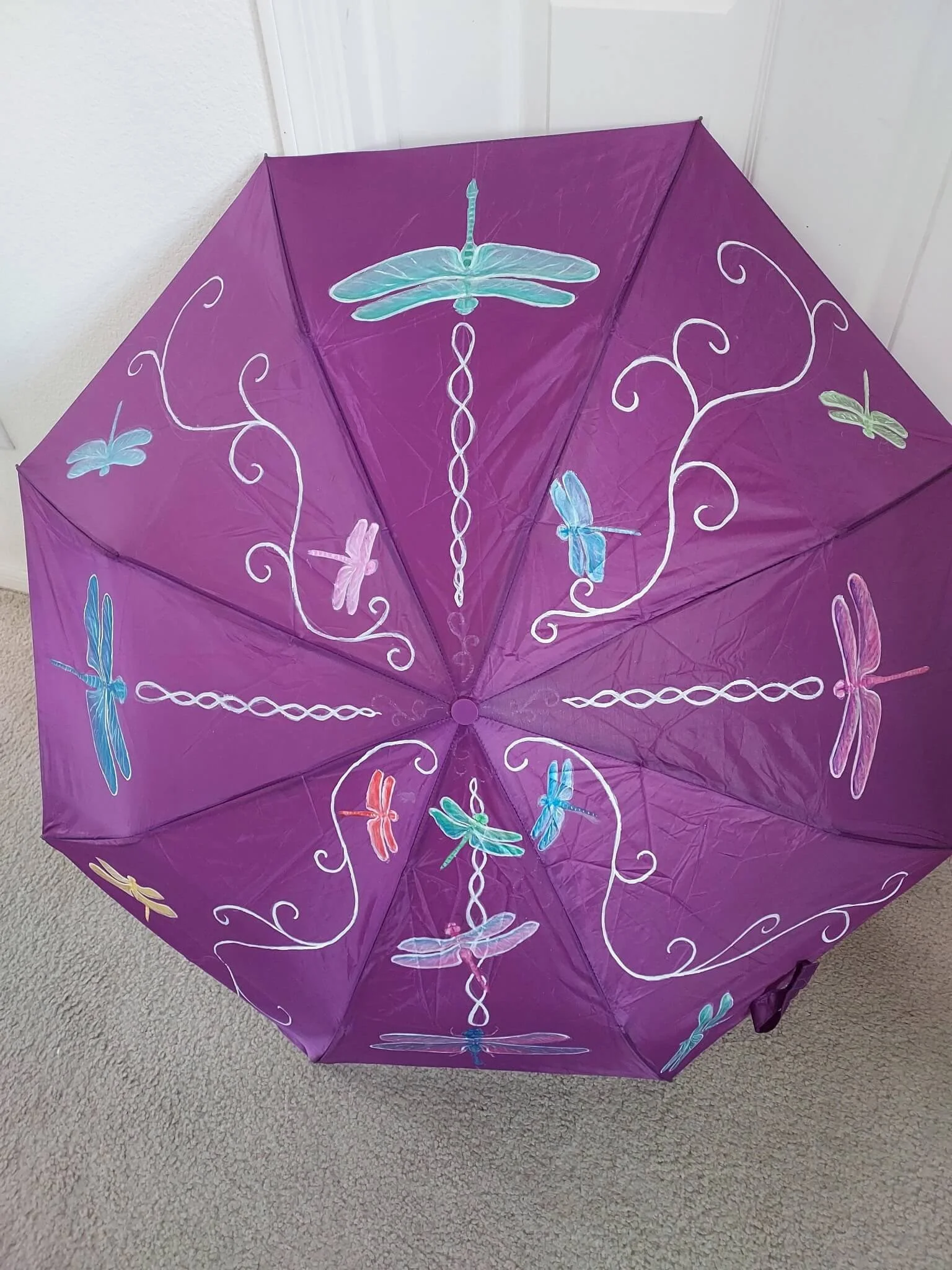 A purple umbrella with colorful dragonfly and butterfly illustrations and white decorative swirls.