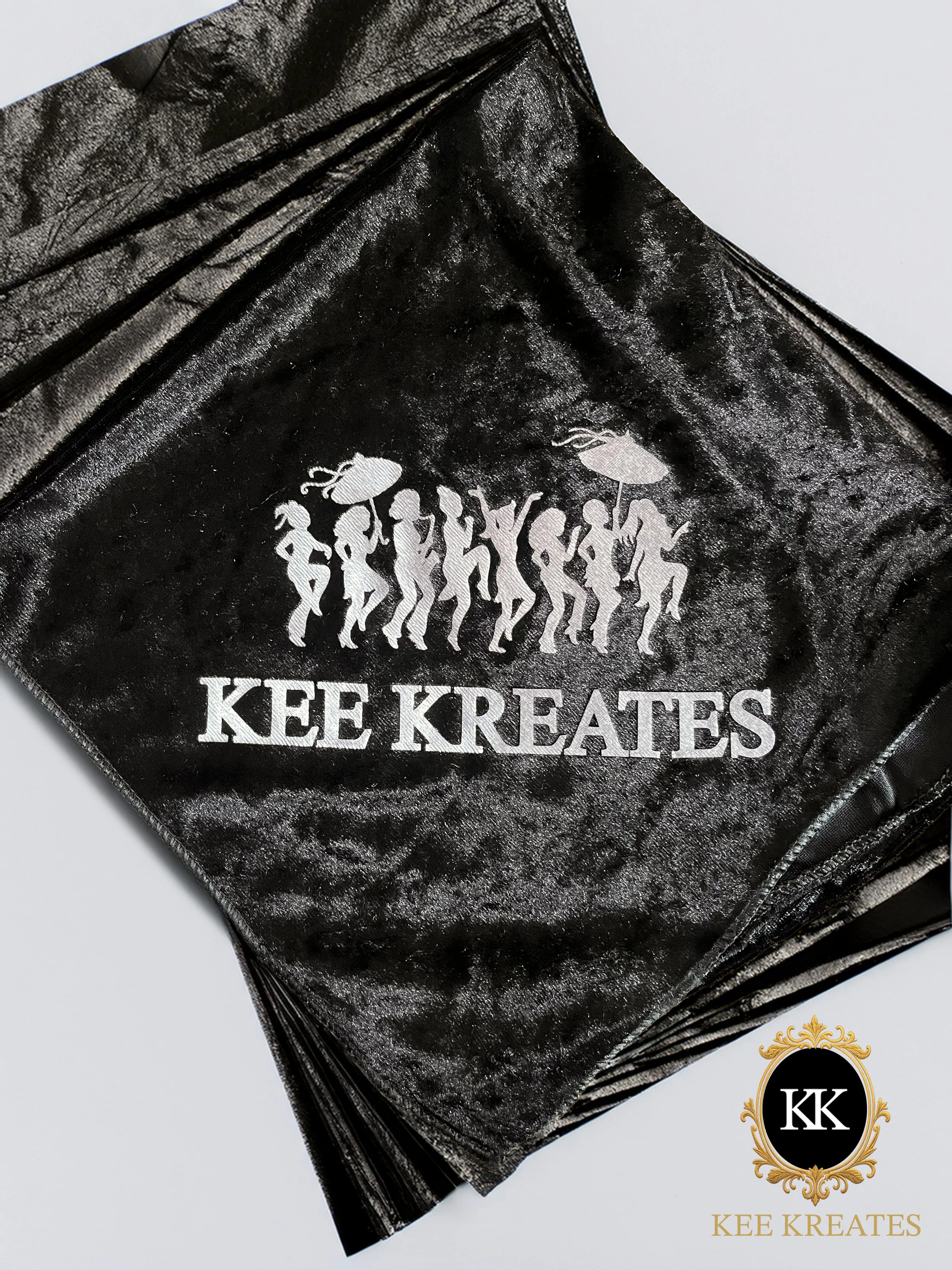 Kee Kreates Photo Booth. Kee Kreates A black satin-like fabric with a white print featuring a line of dancing figures holding umbrellas and the text 'KEE KREATES'.