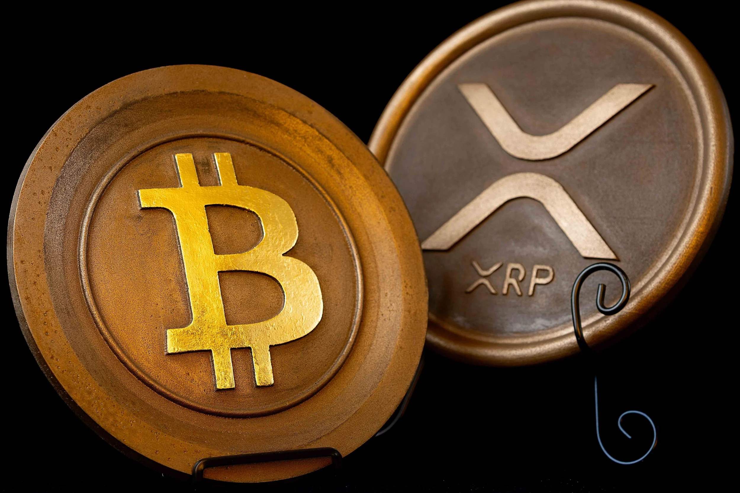 Close-up of physical representations of Bitcoin and Ripple (XRP) cryptocurrencies on black background.