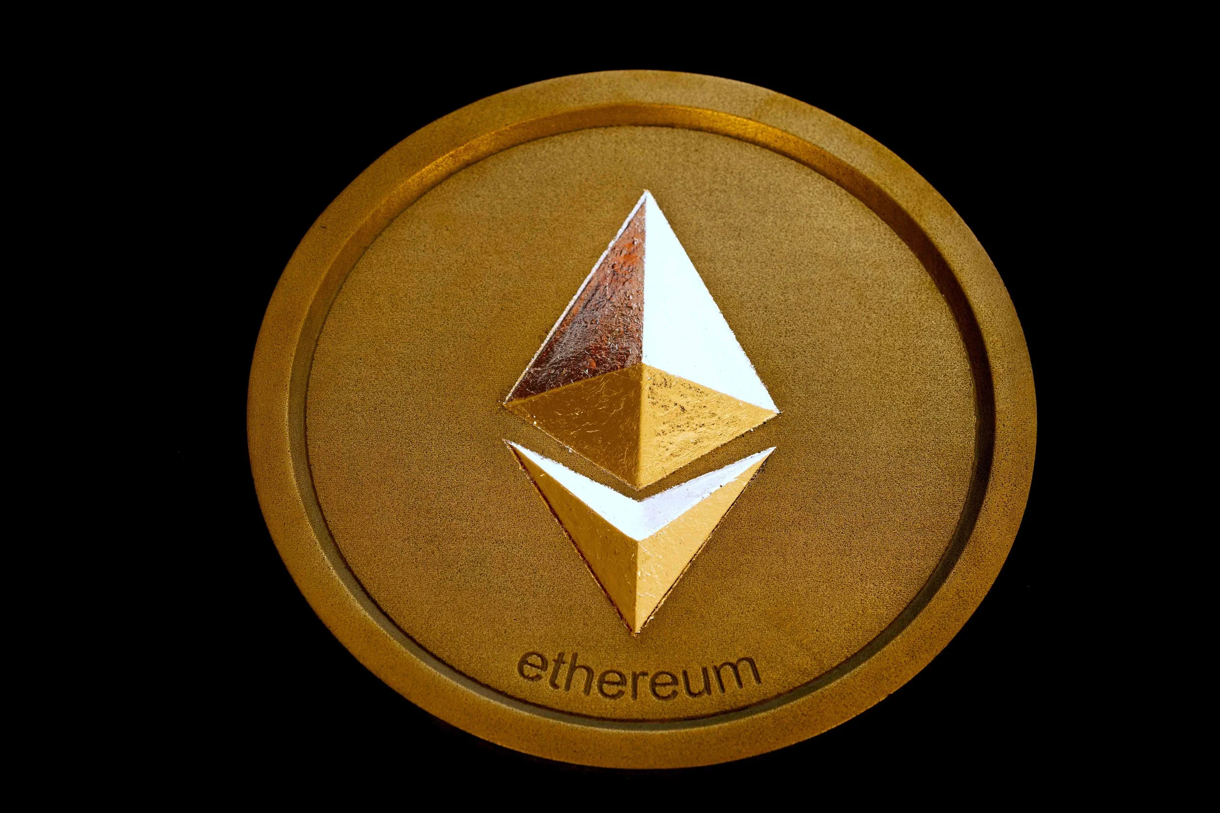 Brass-colored coin featuring the Ethereum crypto, a 3D geometric shape, with the word 'ethereum' printed below.