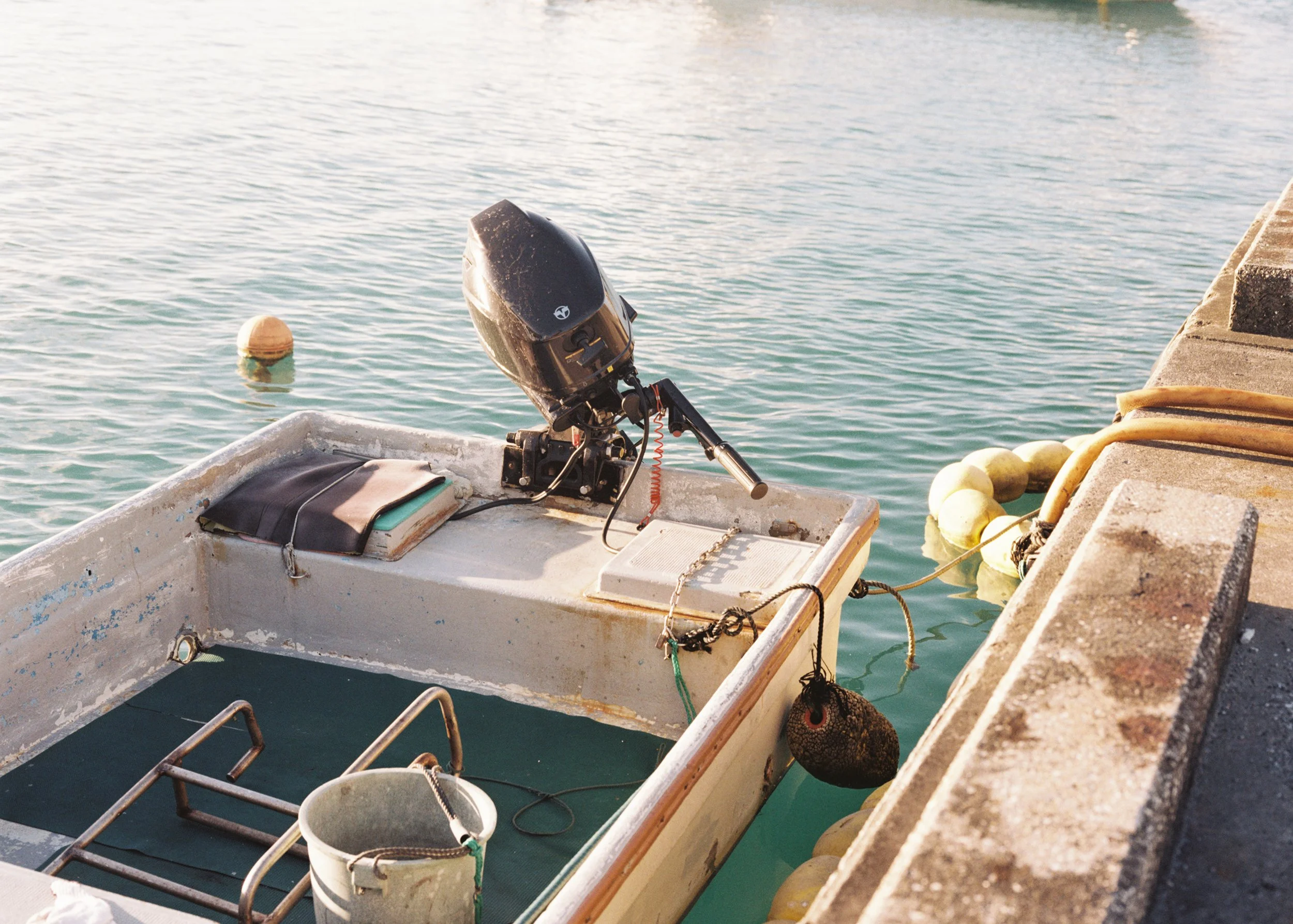 Small white boat with a black outboard motor docked at a pier, with water and a yellow buoy in the background.