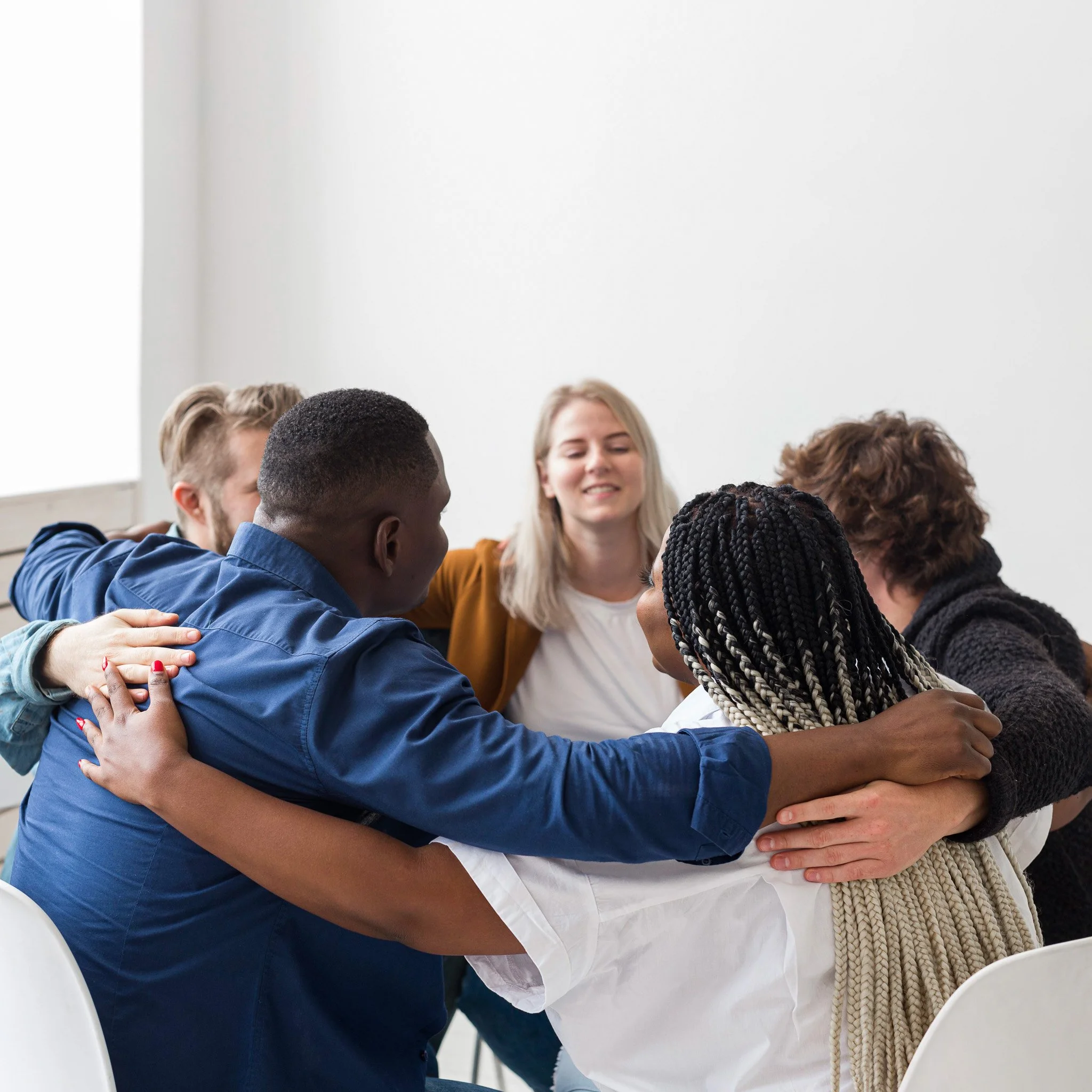 Group of diverse people hugging in a healing circle during an indoor gathering.