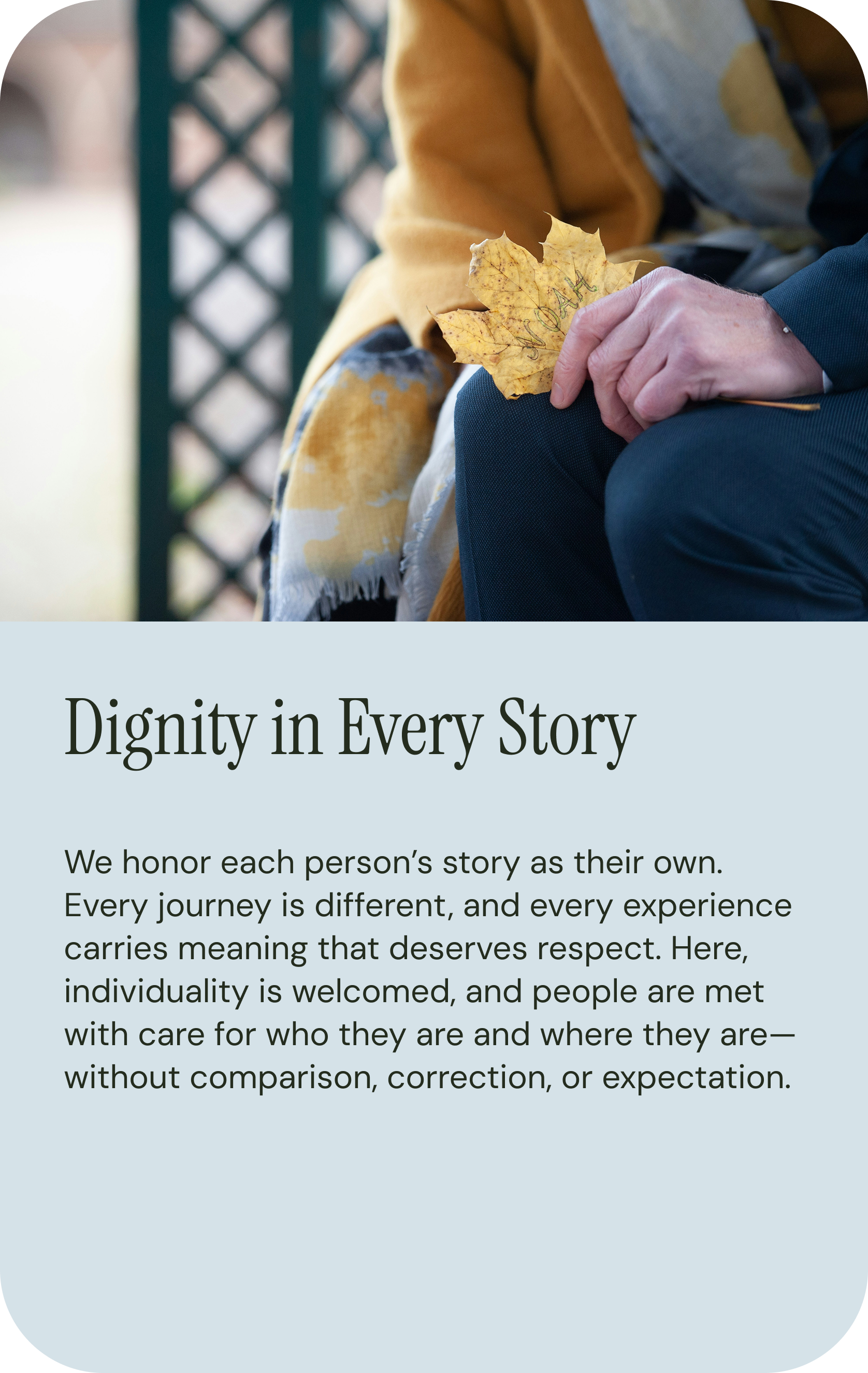 A person holding a yellow leaf with writing, sitting outdoors near a lattice fence, wearing a mustard yellow coat and a scarf, with text about dignity and respect in storytelling.