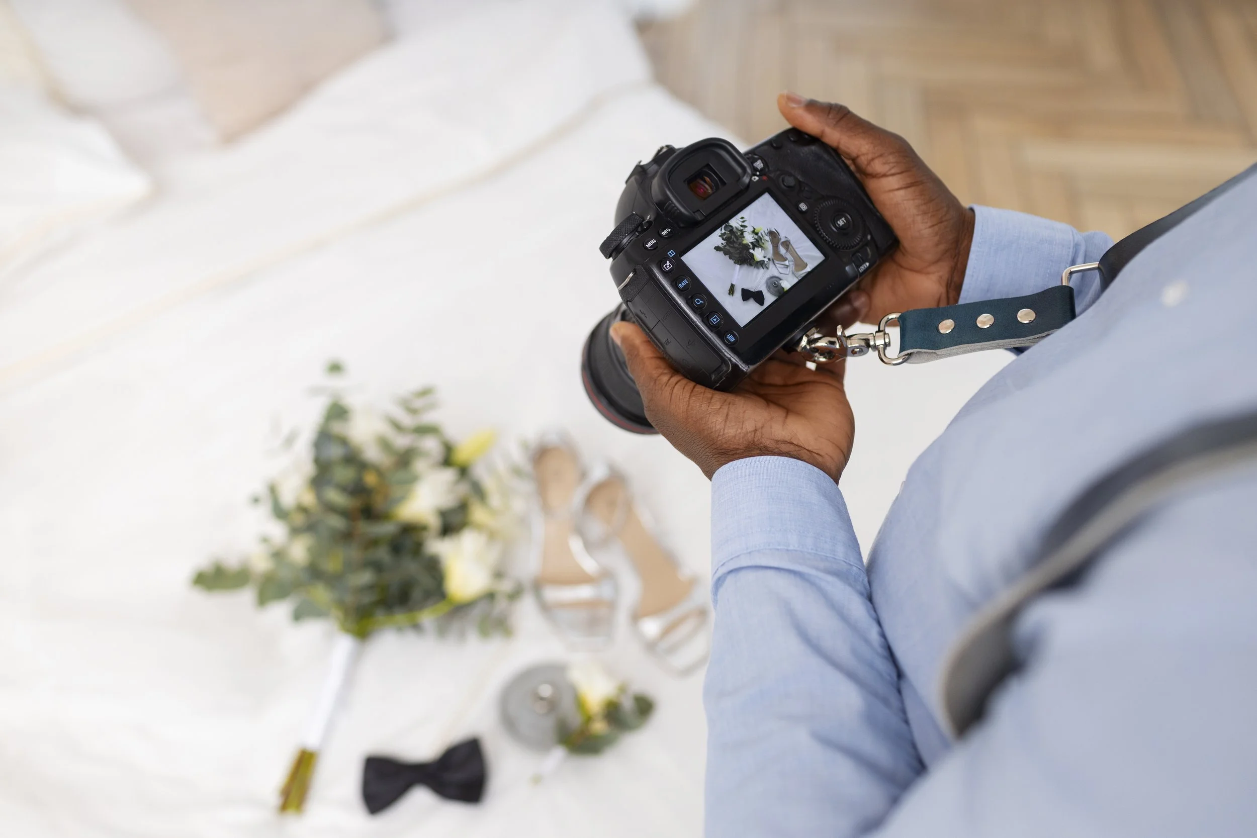 Persona tomando una fotografía de un ramo de flores y accesorios para boda en el suelo con una cámara réflex digital.