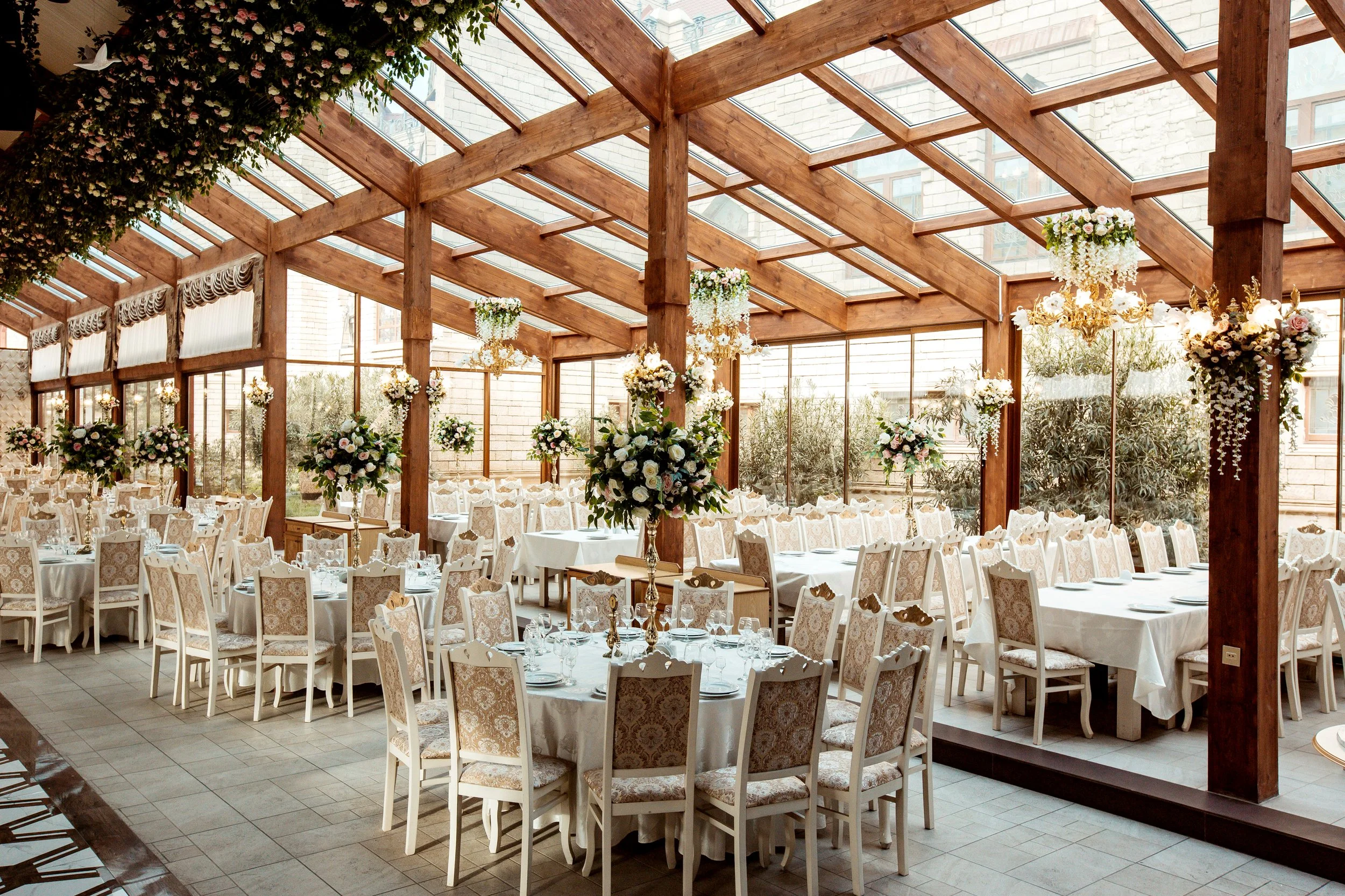 Sala de banquetes decorada con flores y candelabros de estilo elegante en un espacio con estructura de madera y ventanas de vidrio.
