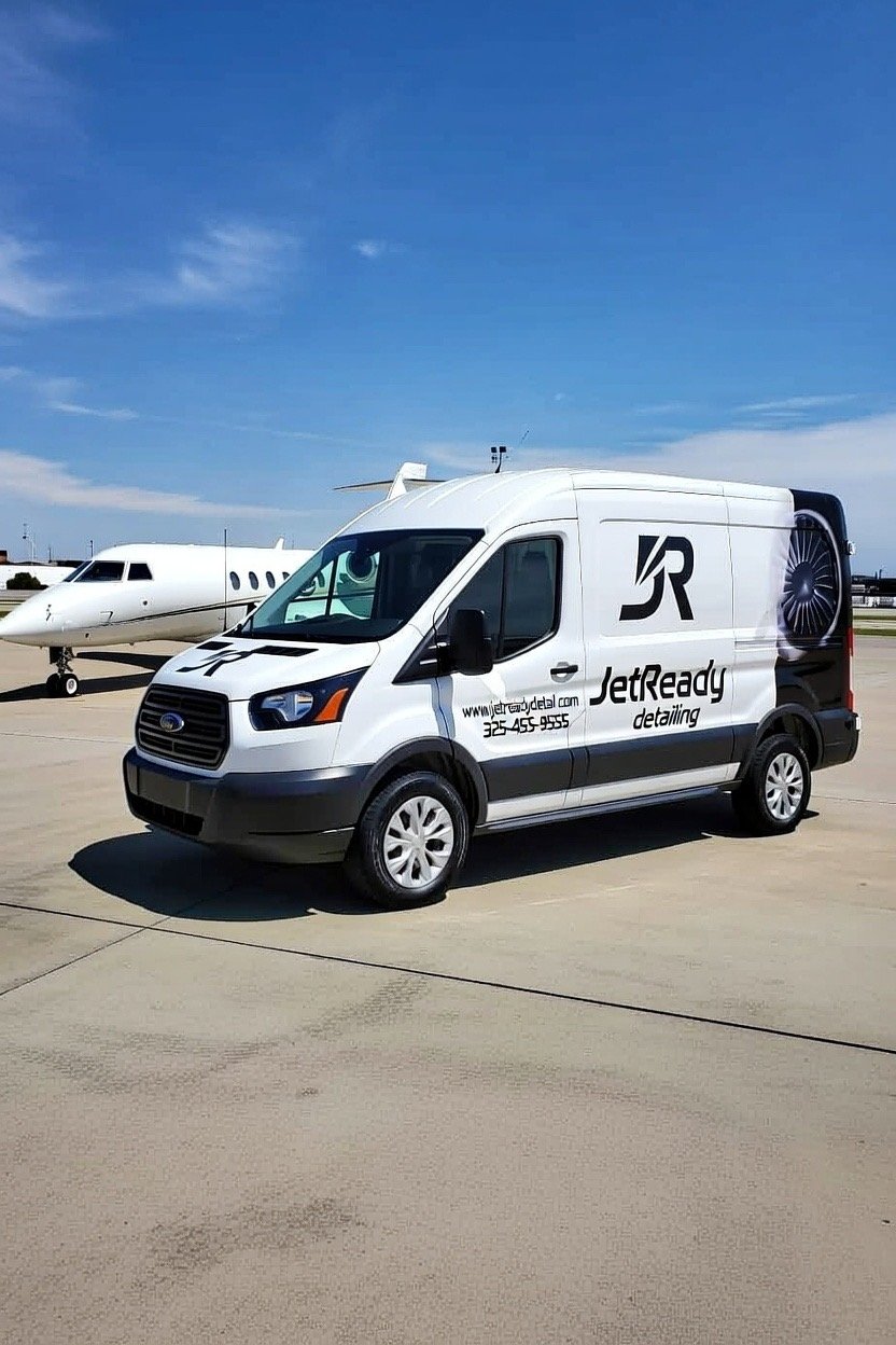 A white JetReadiness detailing van parked on an airport tarmac next to a private jet, with a blue sky overhead.