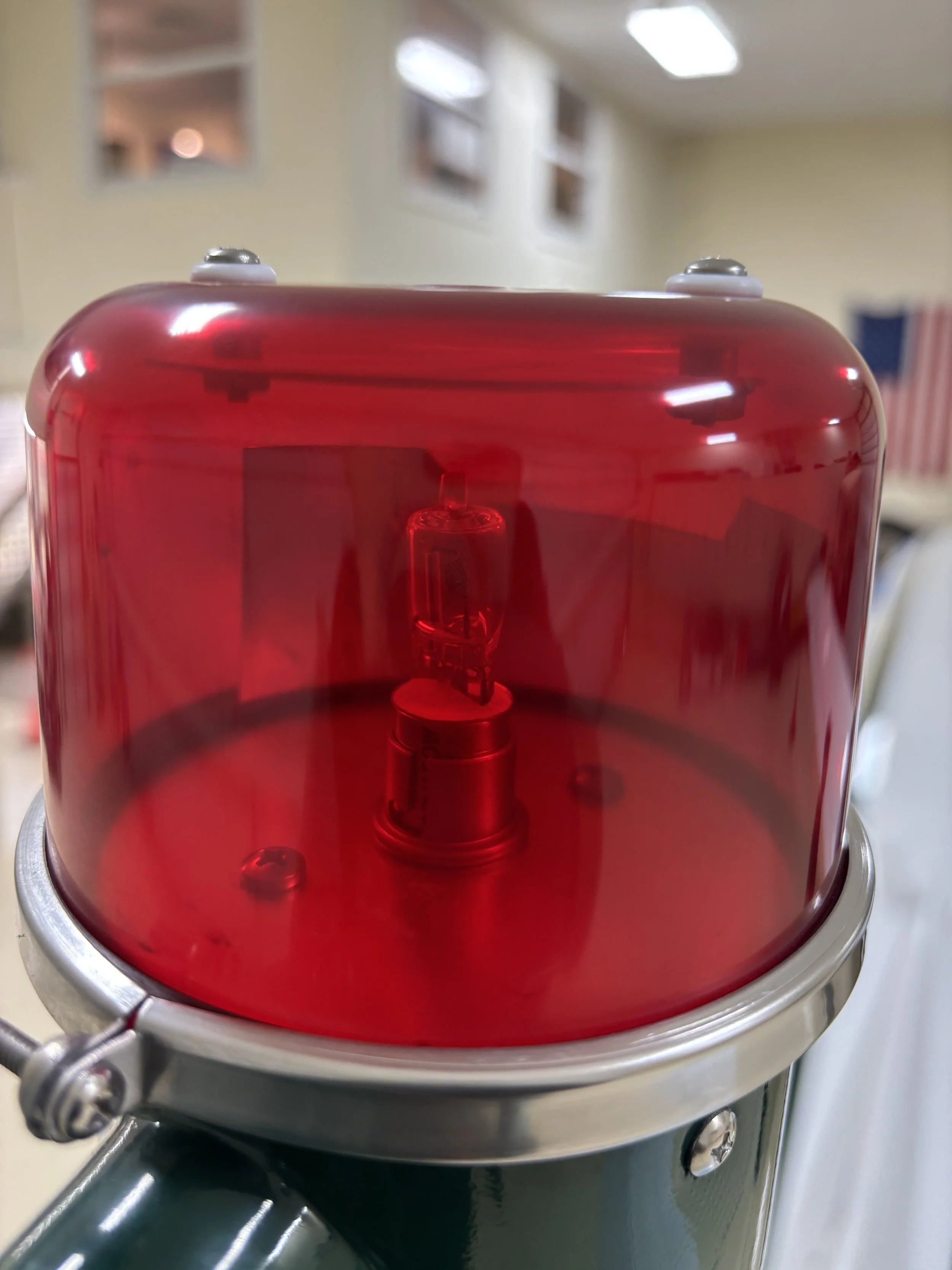 A close-up of a red, translucent, dome-shaped device with internal components visible inside, mounted on a metallic base with bolts.