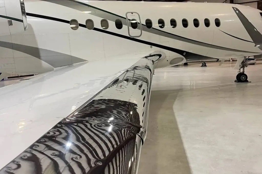 Close-up view of a private jet's wing and fuselage in an airplane hangar.