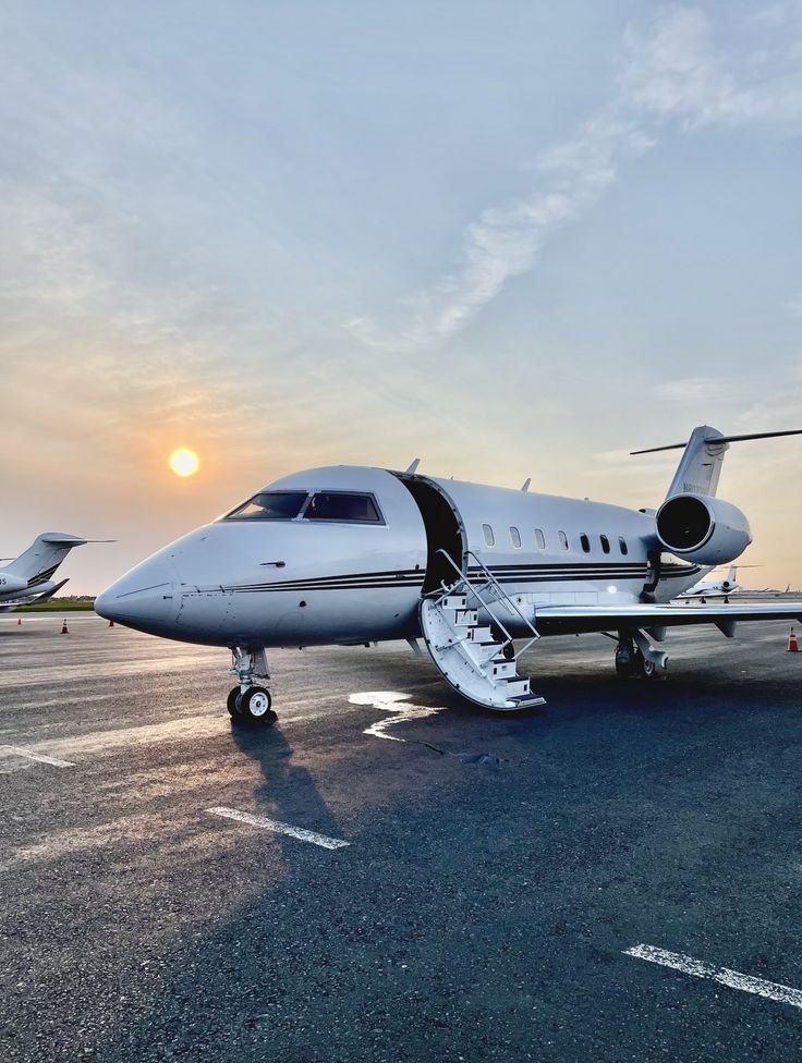 A private jet parked on an airfield during sunset, with stairs leading into the aircraft.