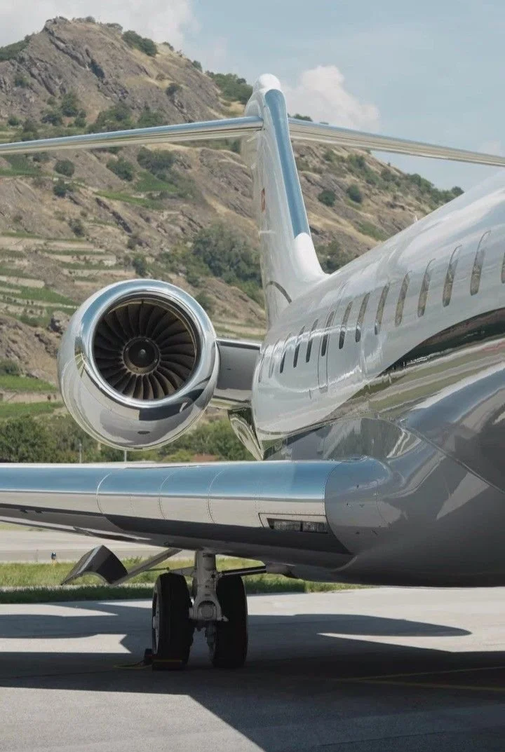 Close-up view of the back of a modern private jet aircraft on the tarmac with a hilly landscape in the background.