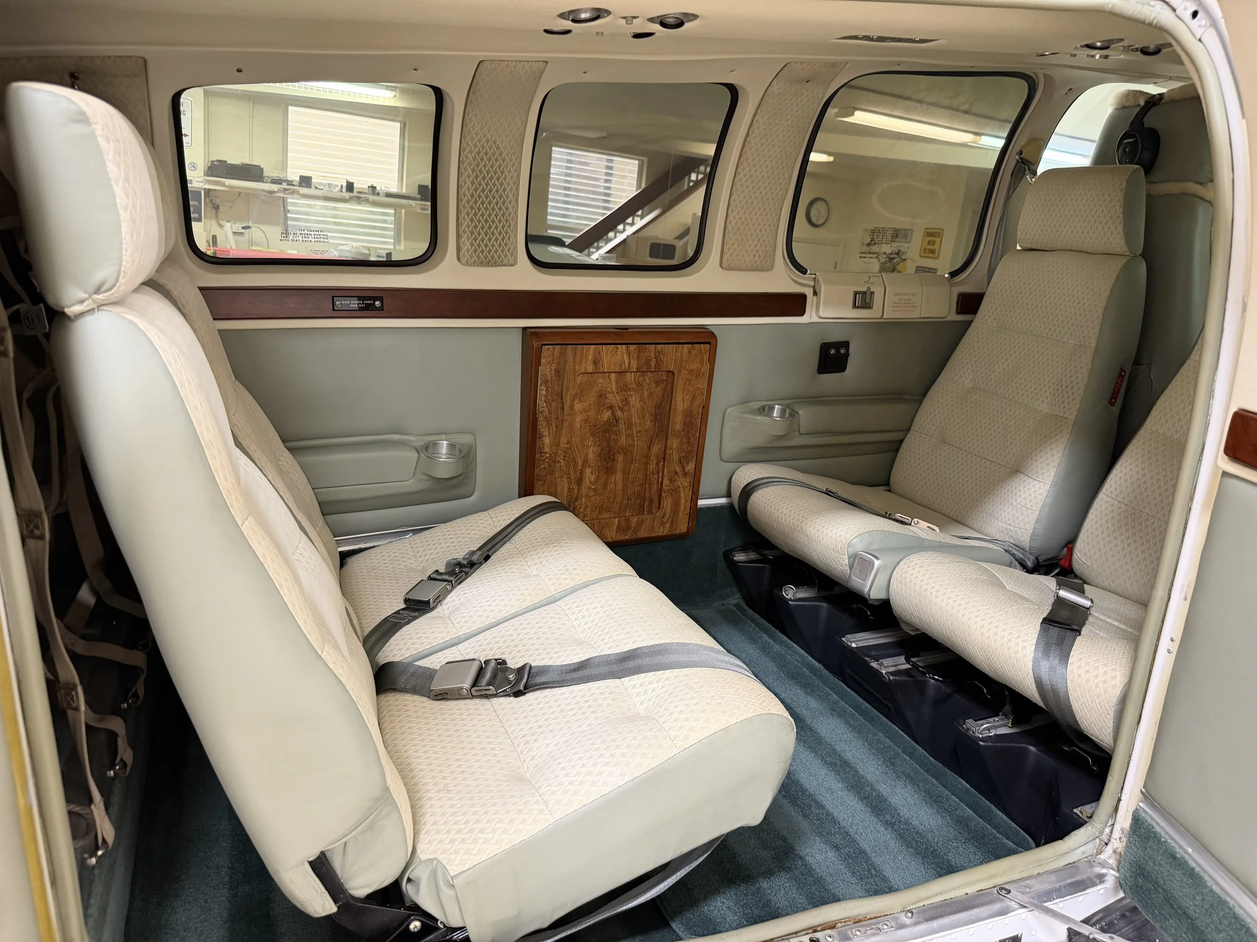 Interior of an airplane, showing two rows of beige passenger seats with seat belts, and large windows along the side of the aircraft.