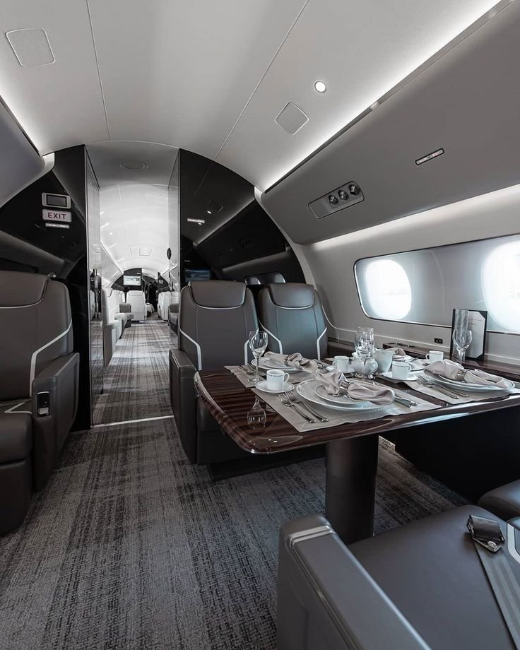 Interior of a private jet with a dining area set for a meal, including a table with plates, glasses, cups, napkins, and cutlery, surrounded by leather seats.