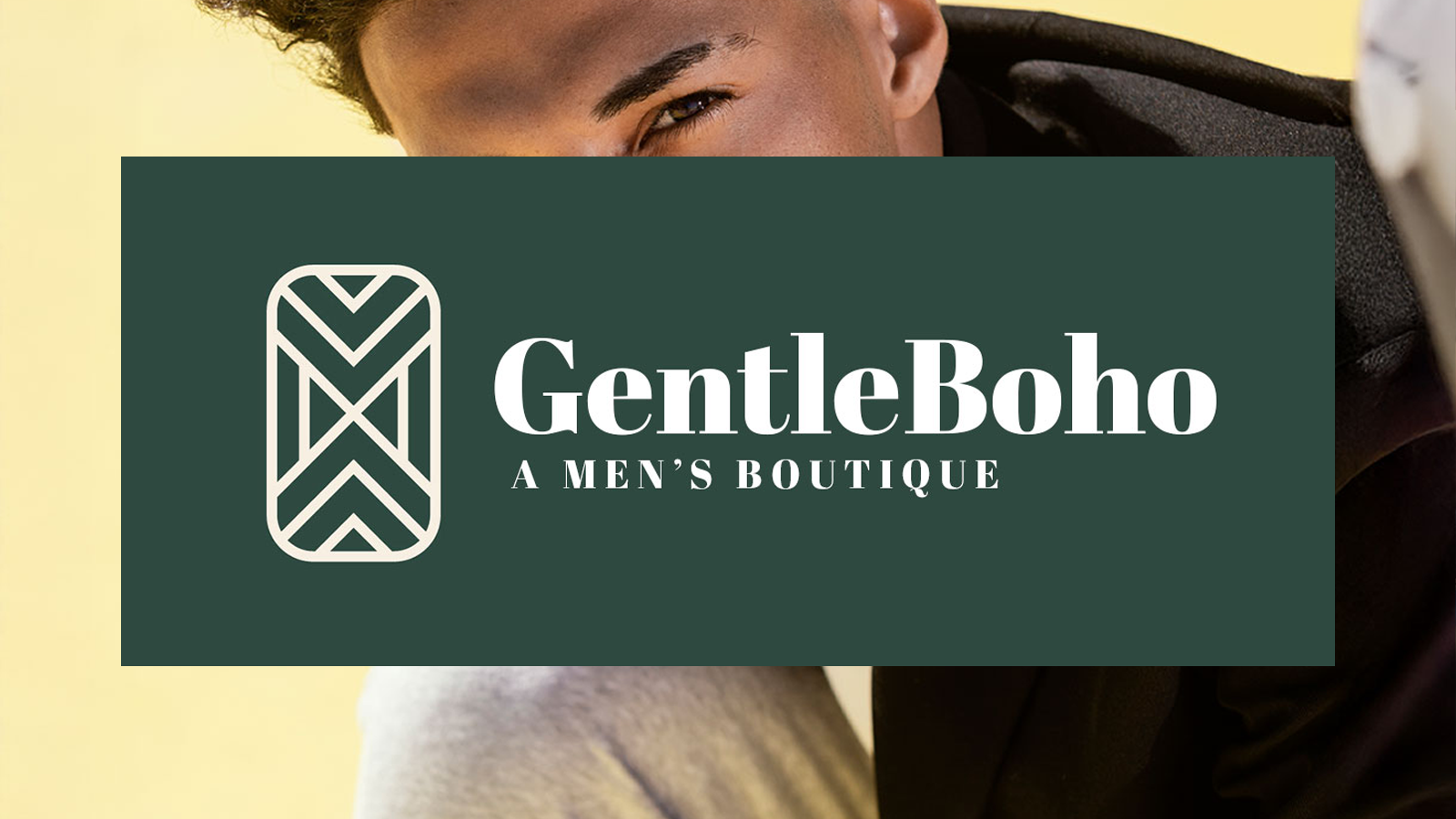 Close-up of a smiling young man with curly hair, wearing a black blazer, in front of a yellow background, with a dark green box overlay containing white logo and text for GentleBoho men's boutique.