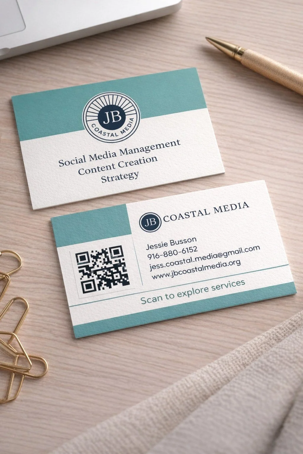 Business cards for Coastal Media and Jessie Busson with contact information and a QR code, placed on a light wooden surface with a pen and paper clips nearby.
