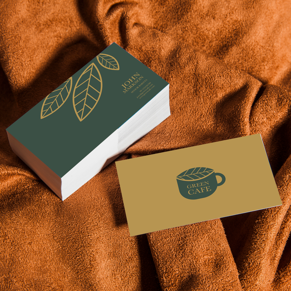 A deck of cards with green leaf design on the back, and a business card with a coffee mug logo and the words "Green Café," placed on a textured orange fabric surface.