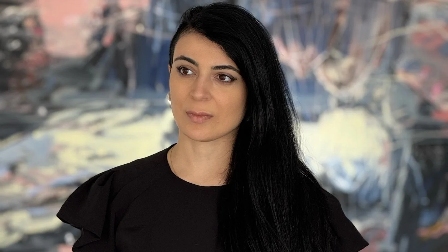 A woman with black hair and a black top standing in front of an abstract, colorful background