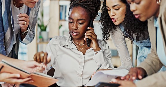 Four women in a meeting discussing documents and a phone.