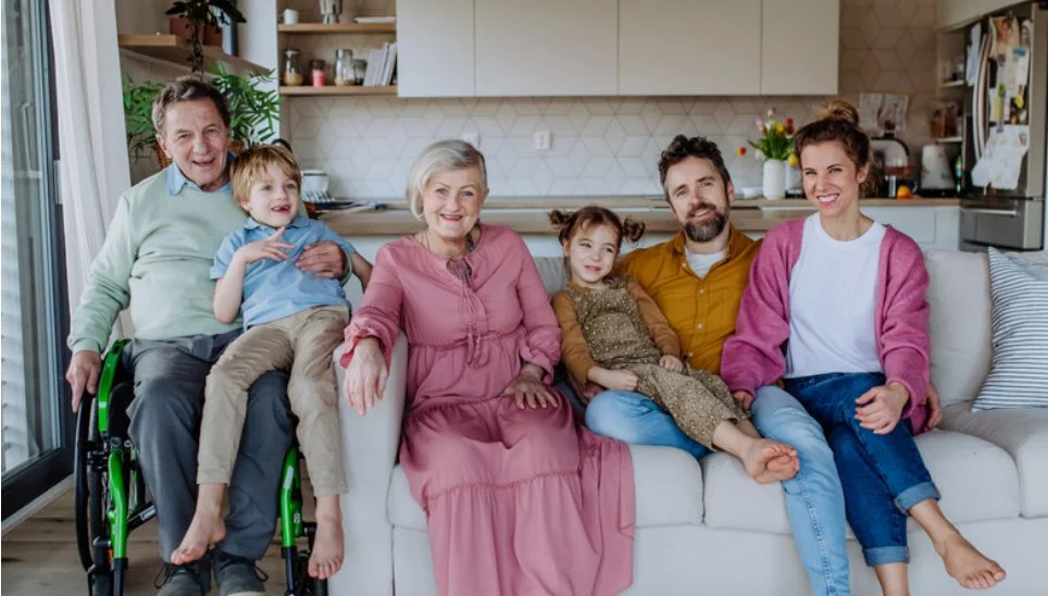 Multigeneration family sitting on a sofa in a modern kitchen, smiling at the camera.