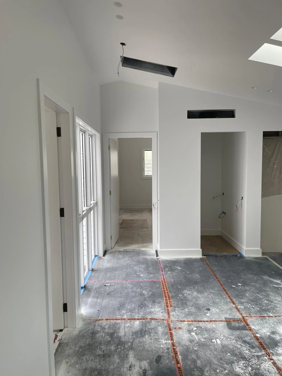 Interior of a house under construction with white walls, drywall openings, and unfinished flooring marked with orange tape.