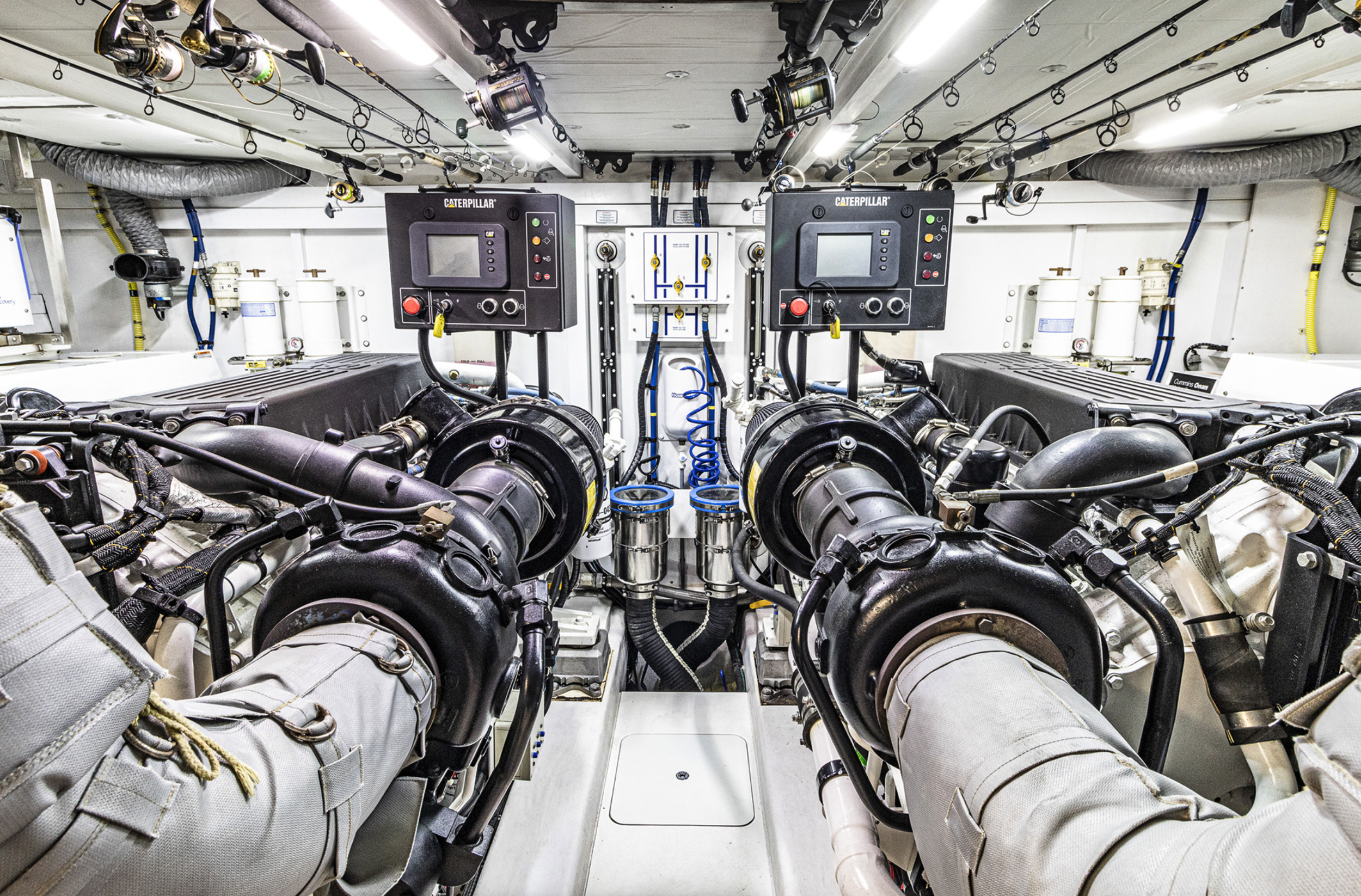 Engine room with two large black engines, control panels, piping, and wires, on a boat or ship.