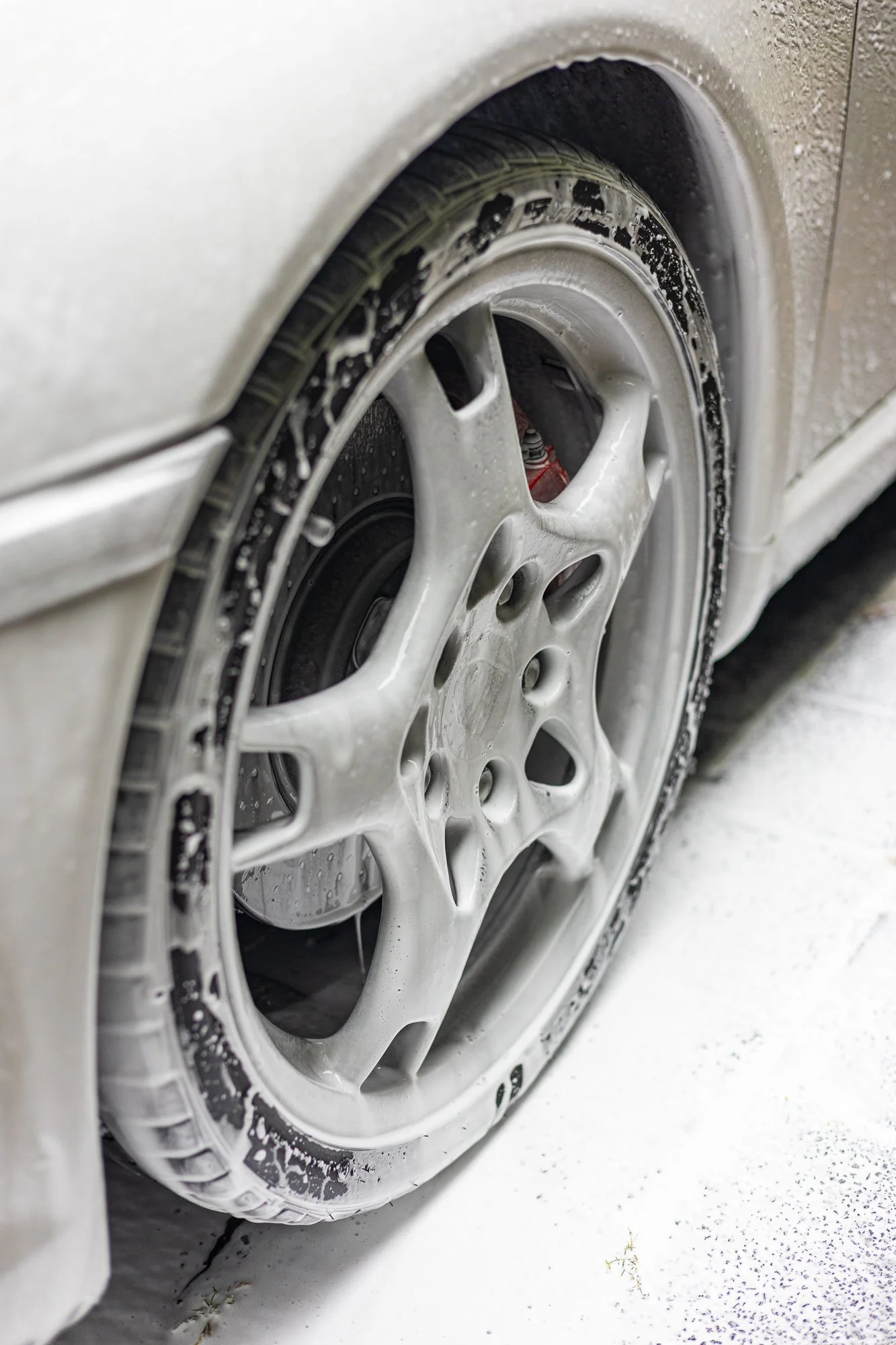 Close-up of a white car wheel with foam soap and water.