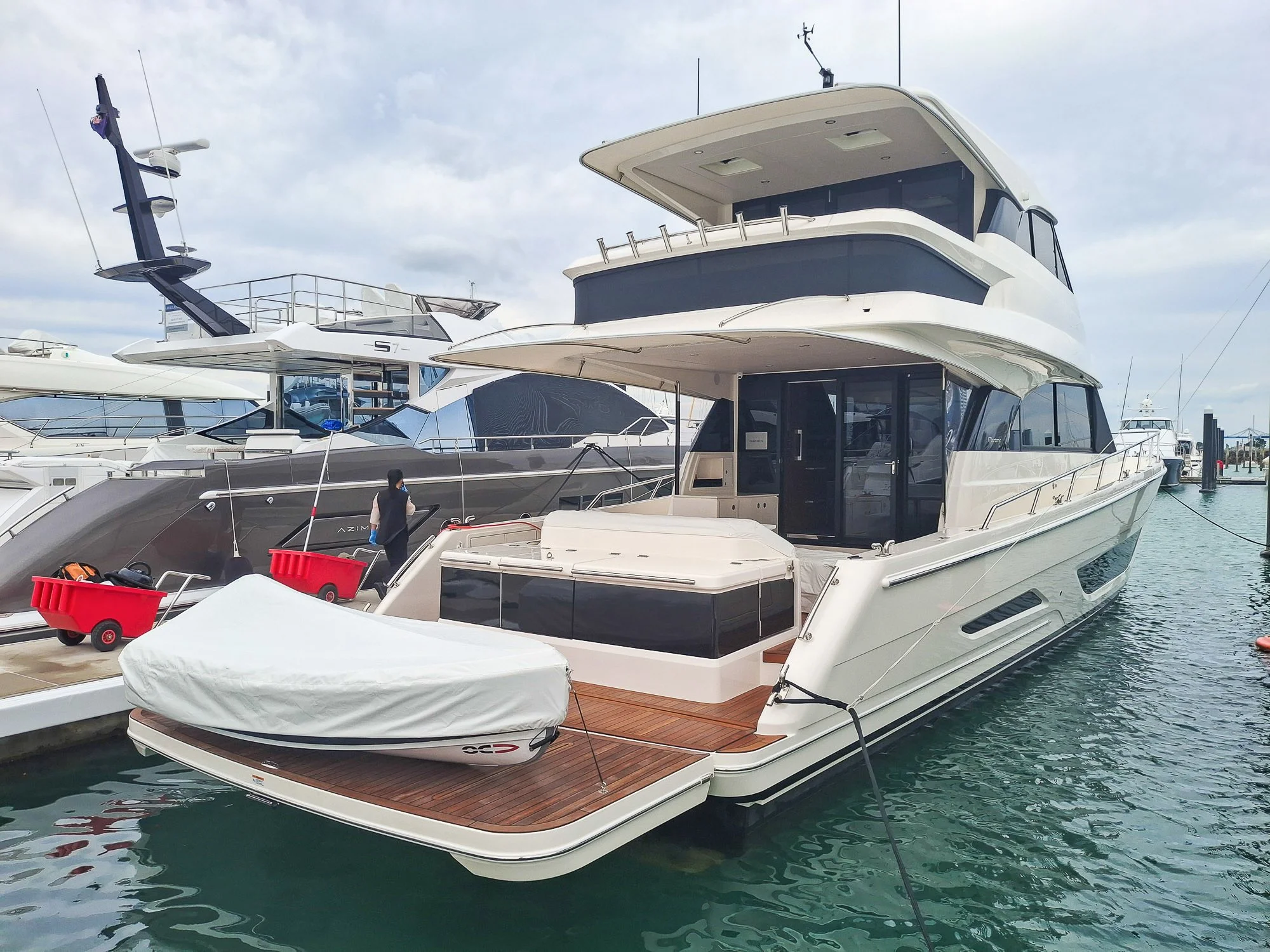 A white yacht docked at a marina surrounded by other boats, with a person cleaning the deck.