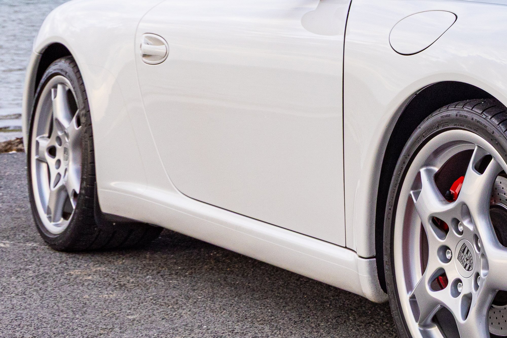 Close-up view of cleaned front side of porsche sports car, showing the front left wheel, tire, and part of the car's body.