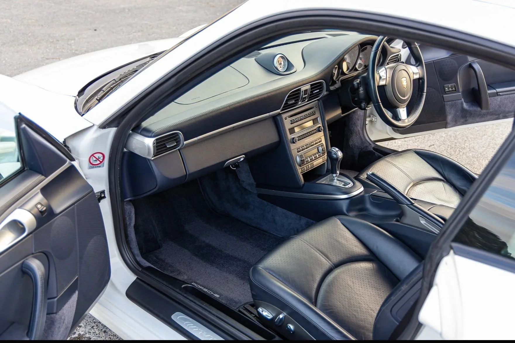 Interior of a white Porsche sports car showing black leather seats, dashboard, steering wheel, gear shift, and center console details.