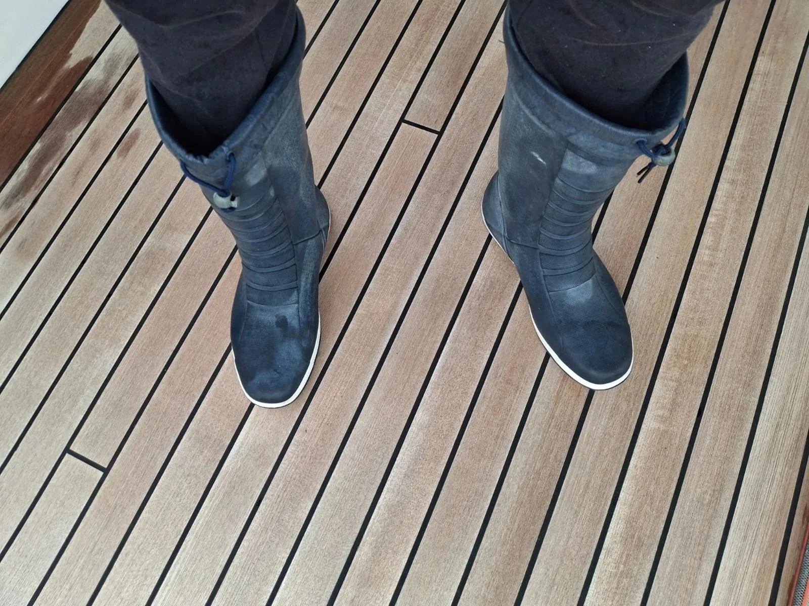 Person wearing black rubber boots standing on wooden deck.