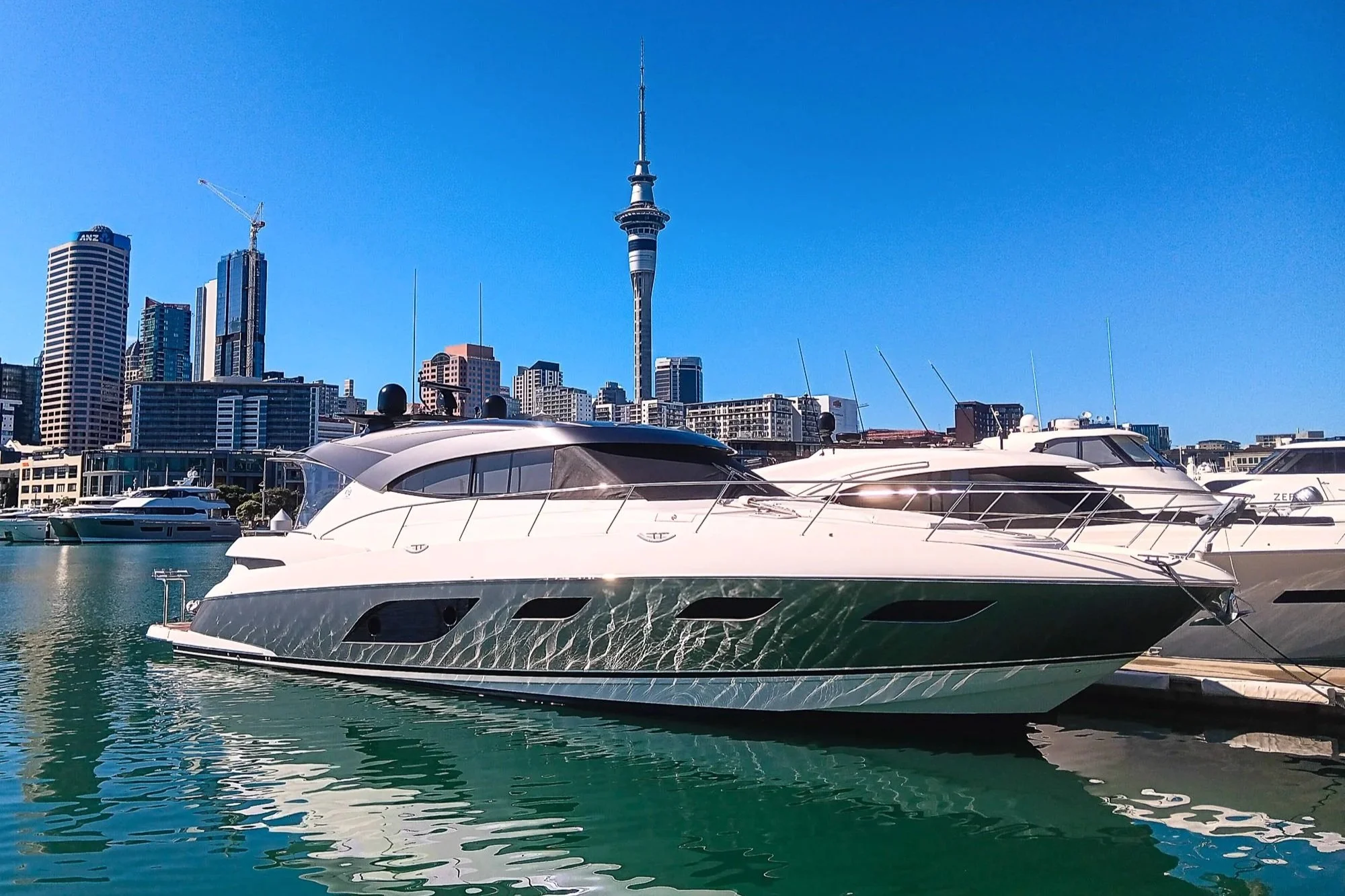 Luxury yacht docked at a marina with city skyline and the Sky Tower in Auckland, New Zealand in the background on a clear sunny day.