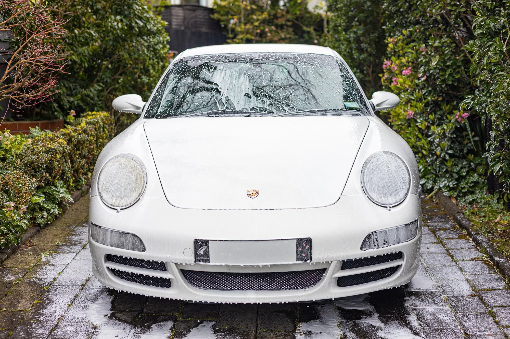 White Porsche sports car being washed on a stone driveway with soap and water.
