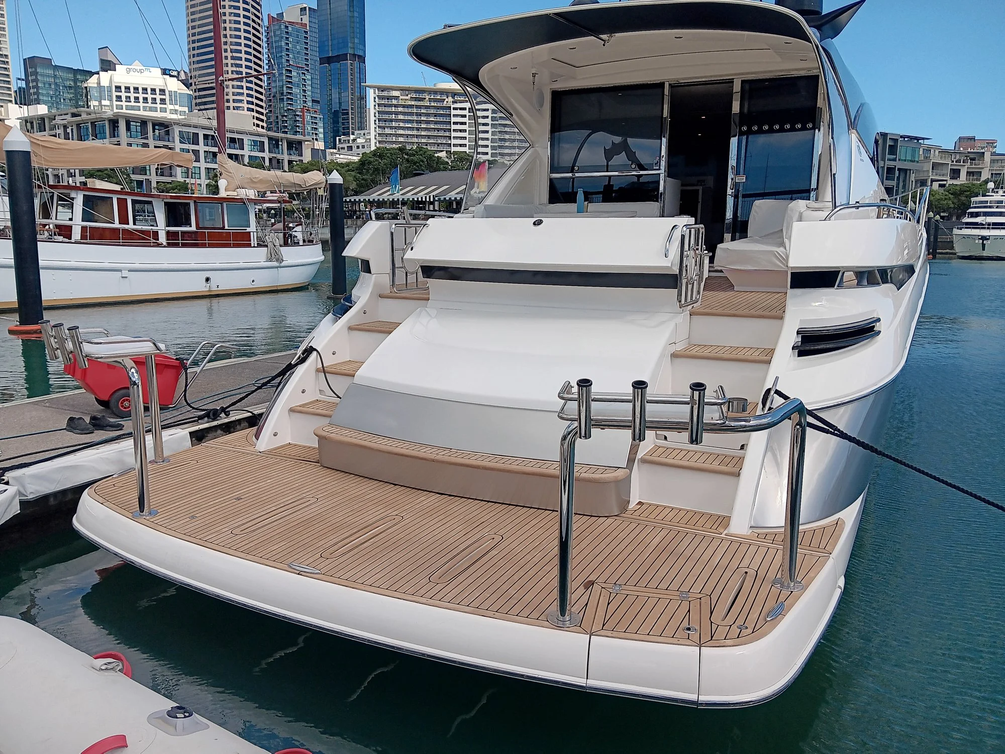 Large white yacht docked at marina with city skyline in background, featuring a spacious deck and modern design.
