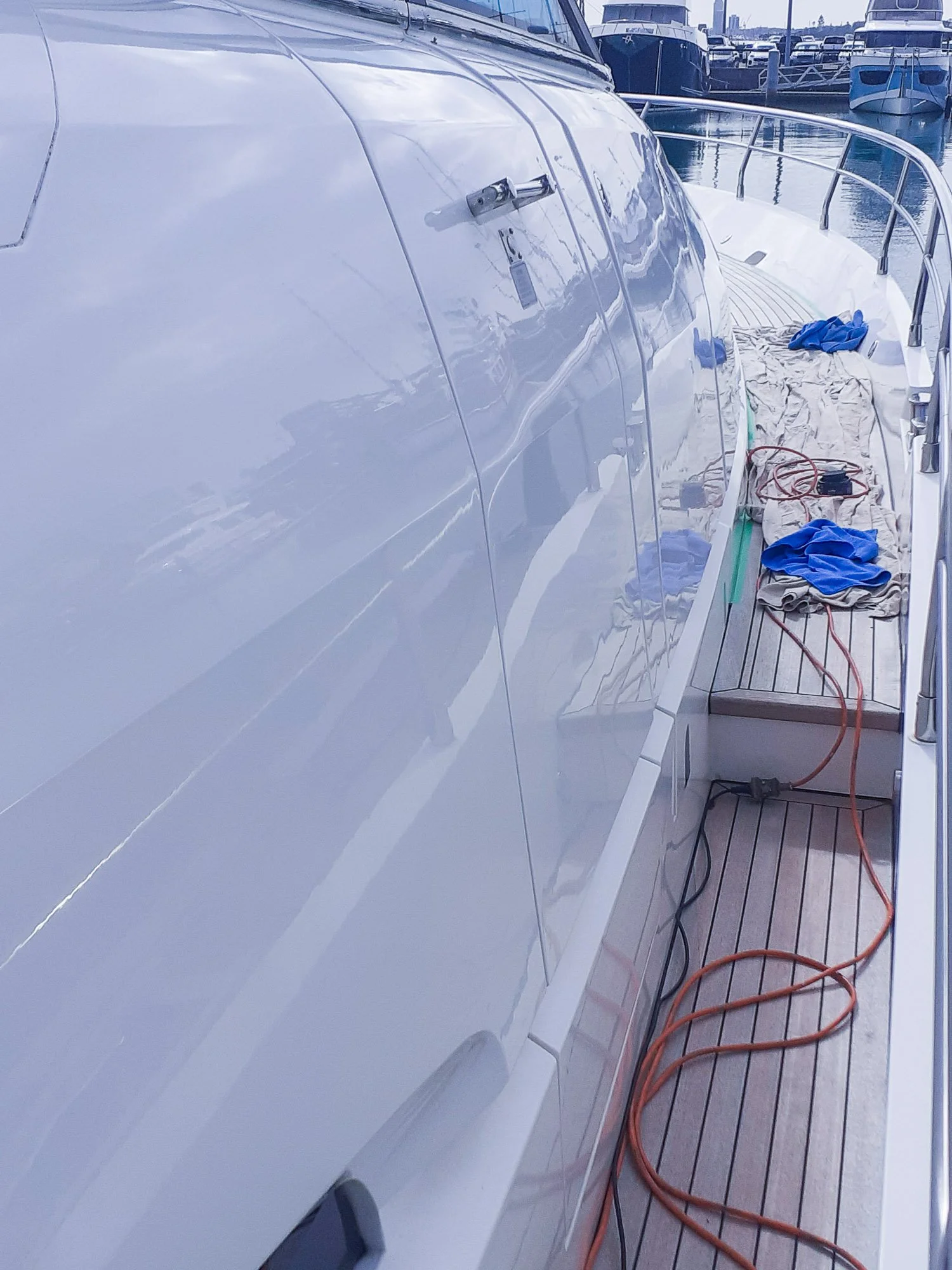 Side view of a white yacht docked at a marina, with cleaning supplies and electrical cords on the wooden deck.