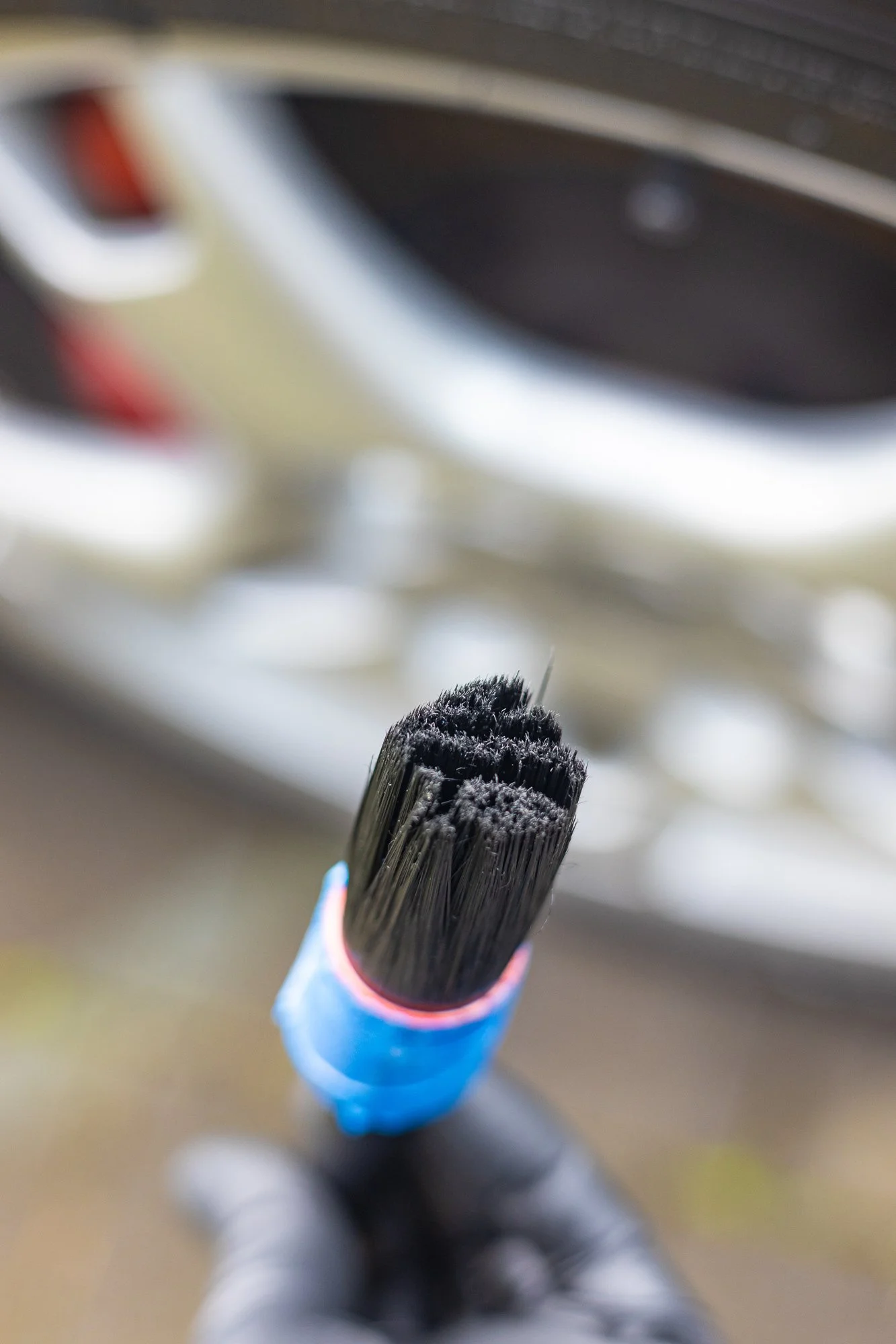 Close-up of a detail brush with black bristles, held by a hand wearing a black glove.