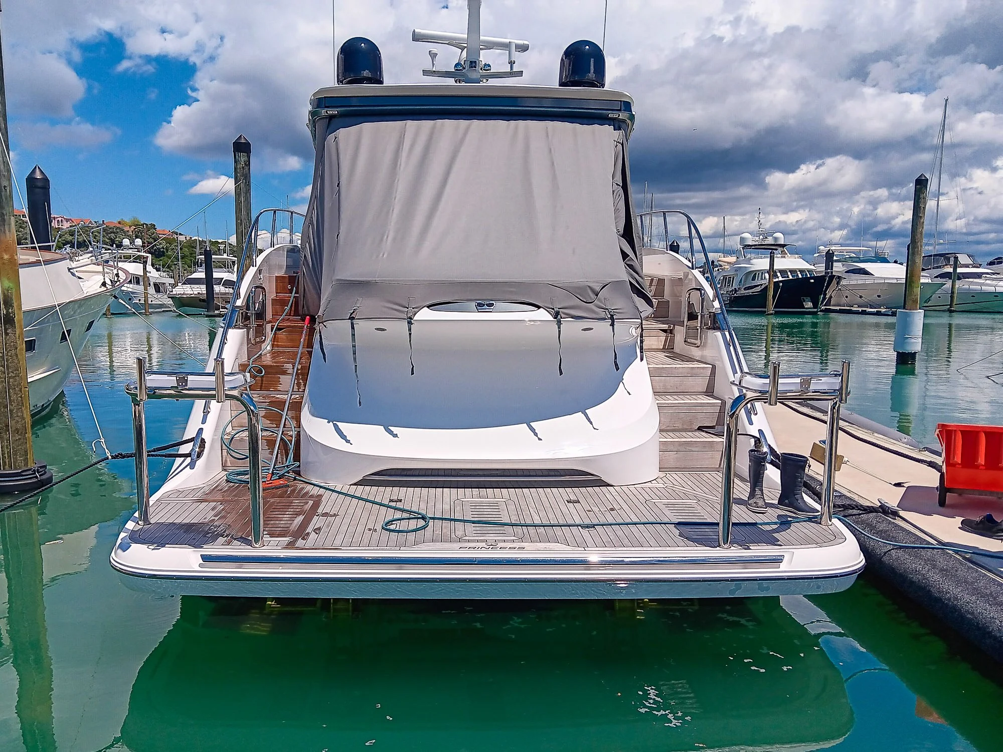 A large white yacht docked at a marina with other boats in the background, under partly cloudy skies.