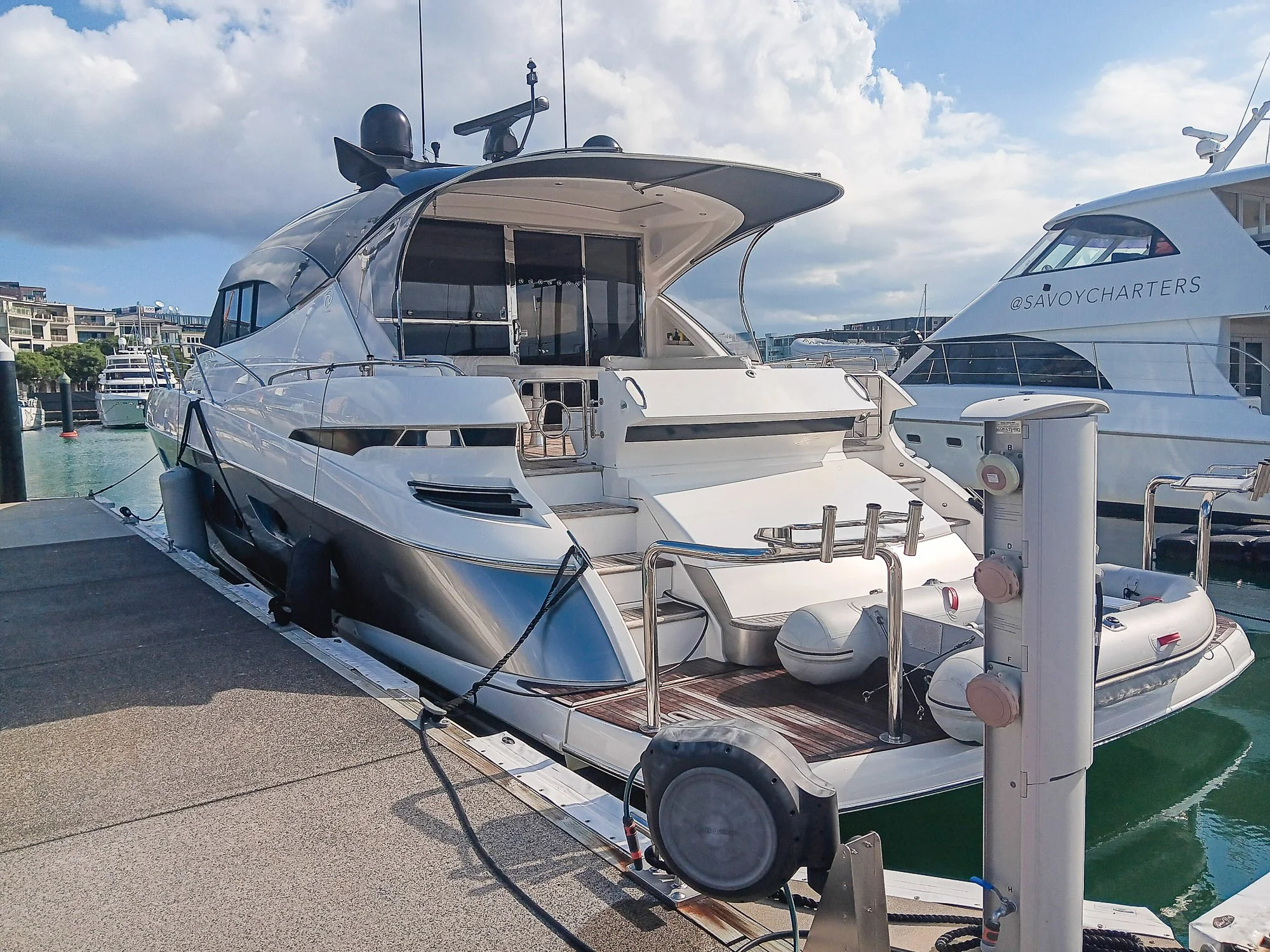 Luxury white yacht docked at marina with buildings and other boats in background.