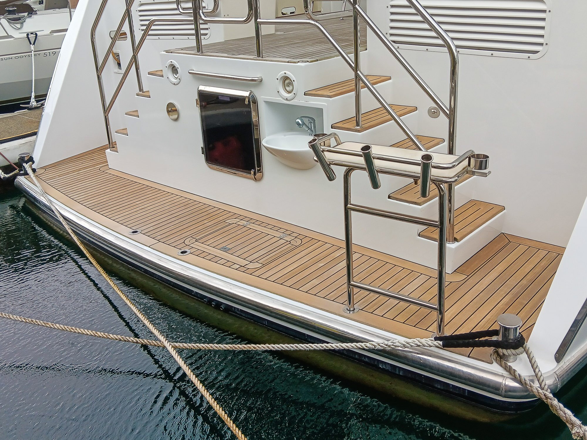 Close-up view of the stern of a luxury yacht, featuring teak decking, railing, stairs, and a small sink.