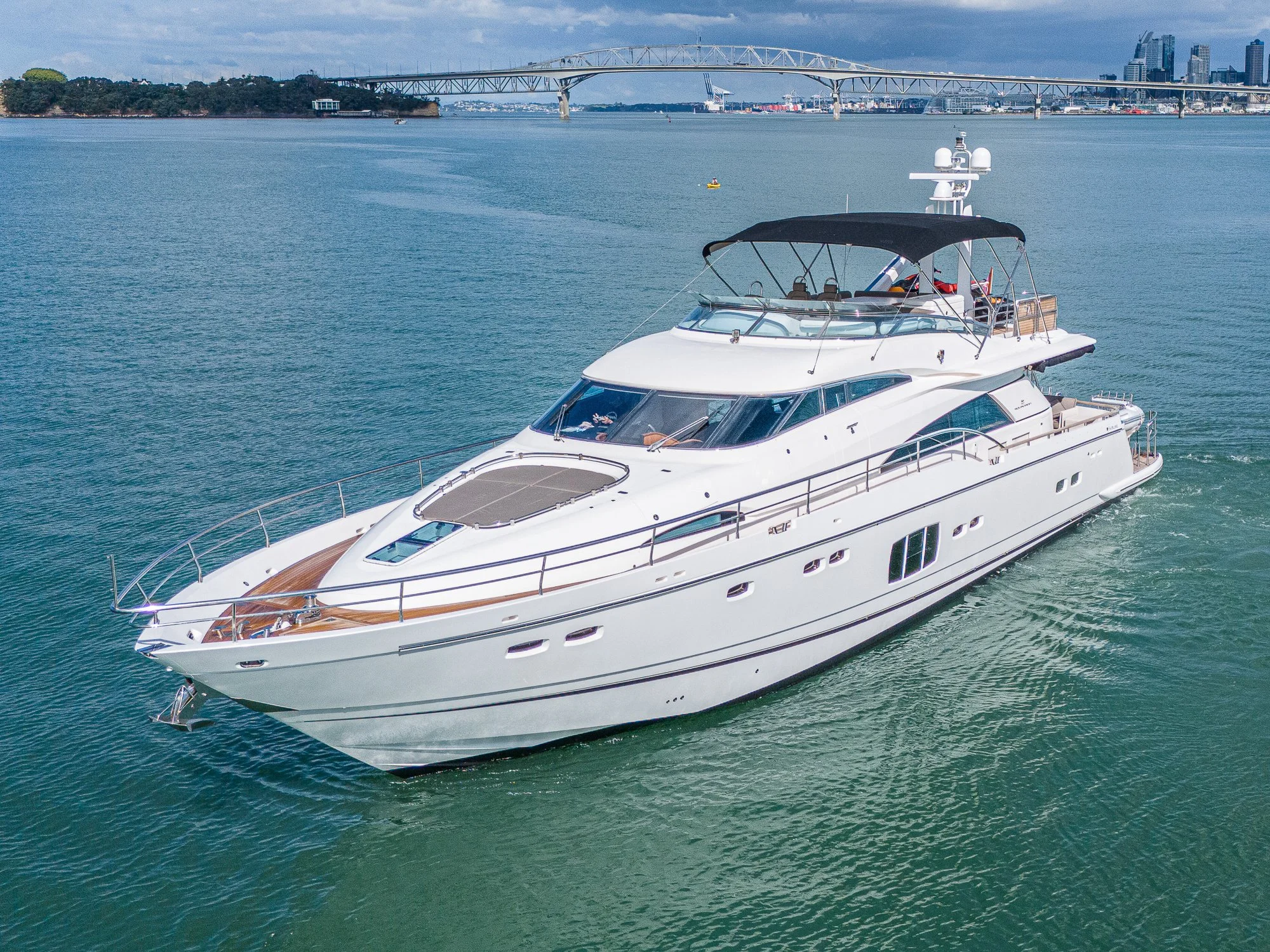 A white luxury yacht cruising on calm water with a city skyline and a bridge in the background.