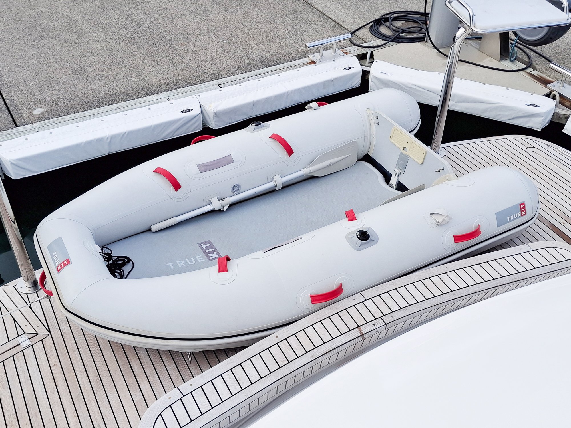 Inflatable boat with red handles on a wooden dock, with a portion of a boat deck and equipment visible.