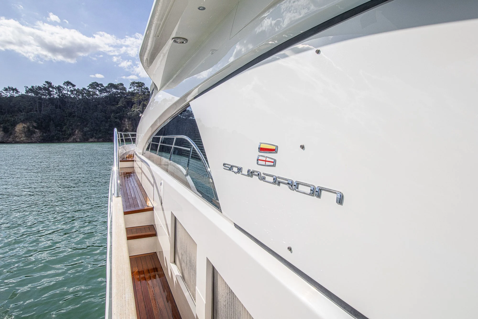 Close-up of a white yacht with the brand name Normandy and emblem, moored on calm water with a forested shoreline in the background.